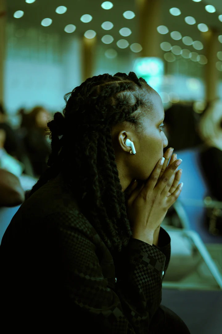 Person with braided hair and an earbud, hands clasped, listening