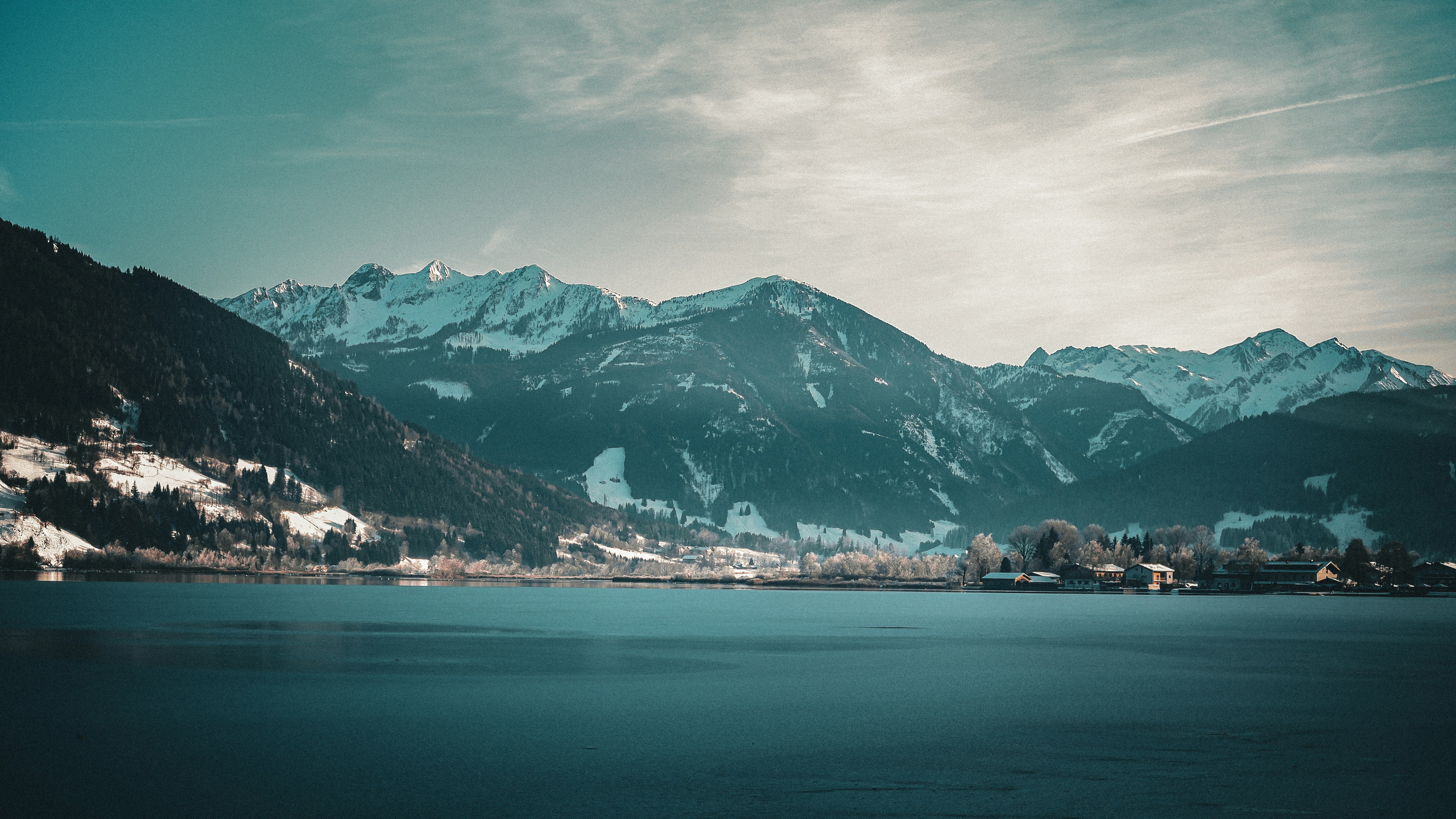 A serene lake with snow-capped mountains and a village