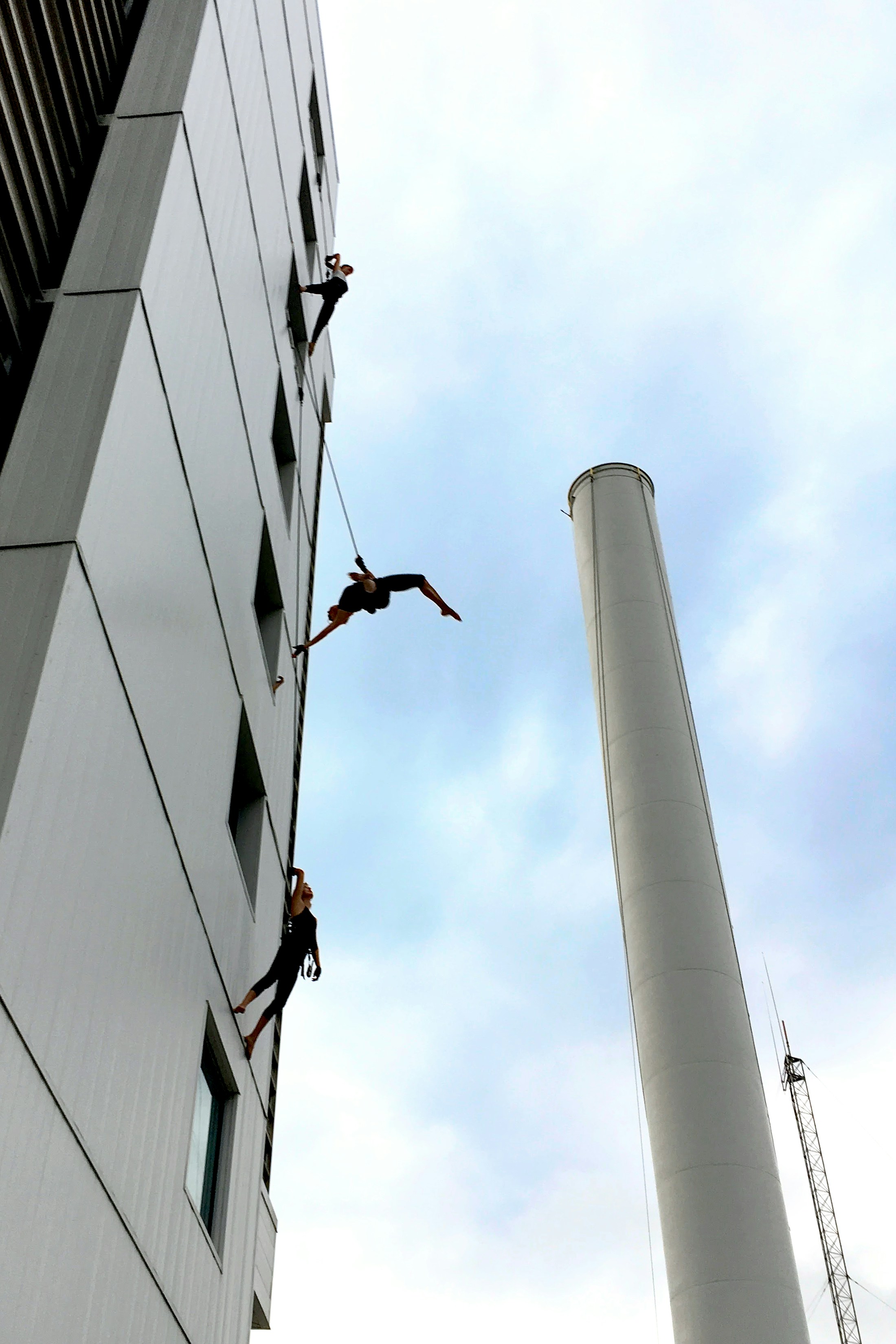 Trois personnes descendant en rappel un bâtiment à côté d’une haute cheminée.