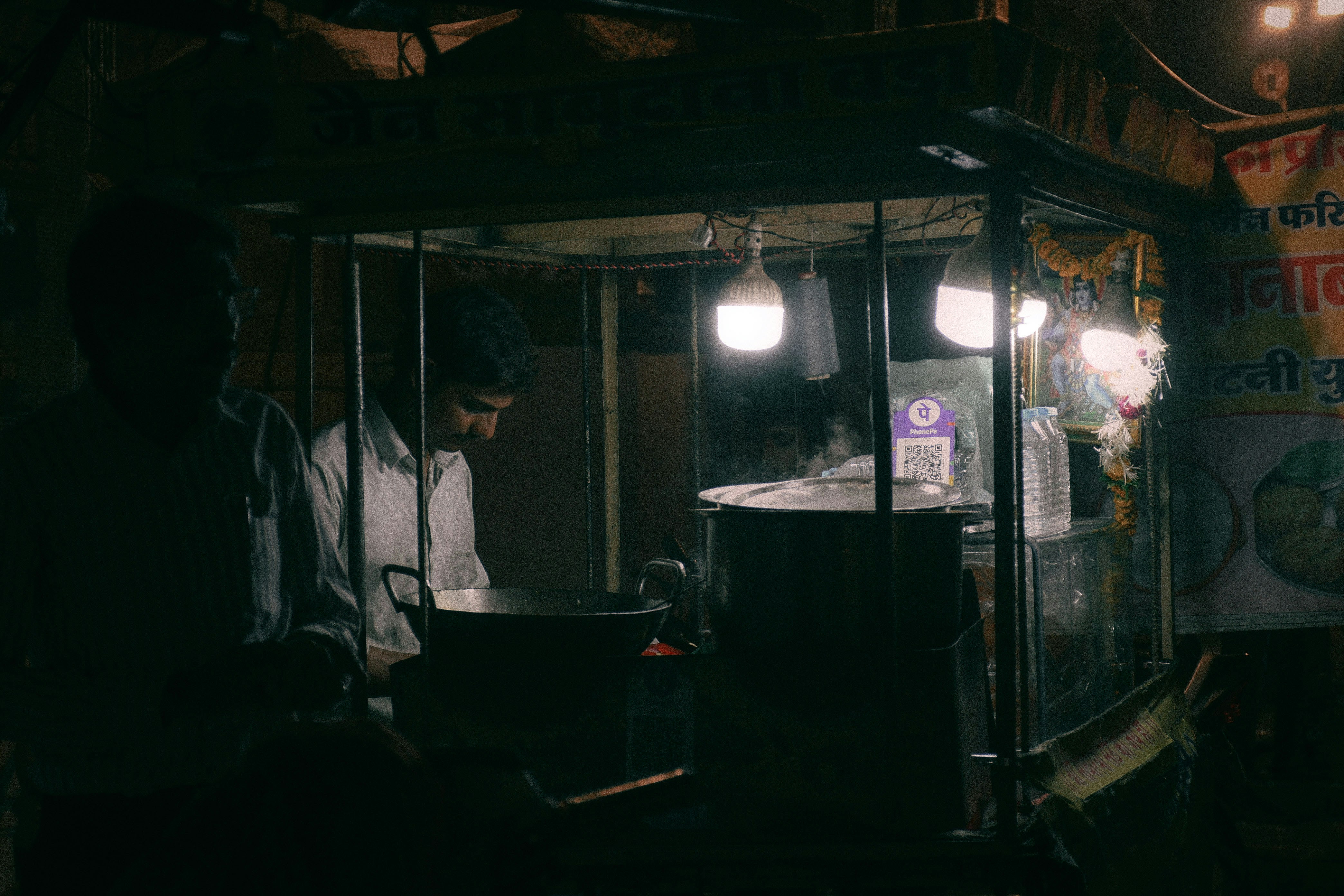 A realistic image of a typical bustling Indian tea stall with a few people discreetly talking in a corner, looking ordinary yet engaged in hushed conversation.