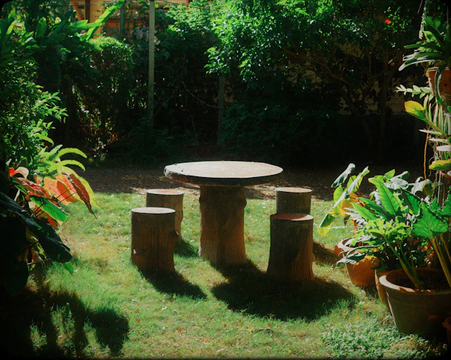 A stone table and stools sit in a sunny garden