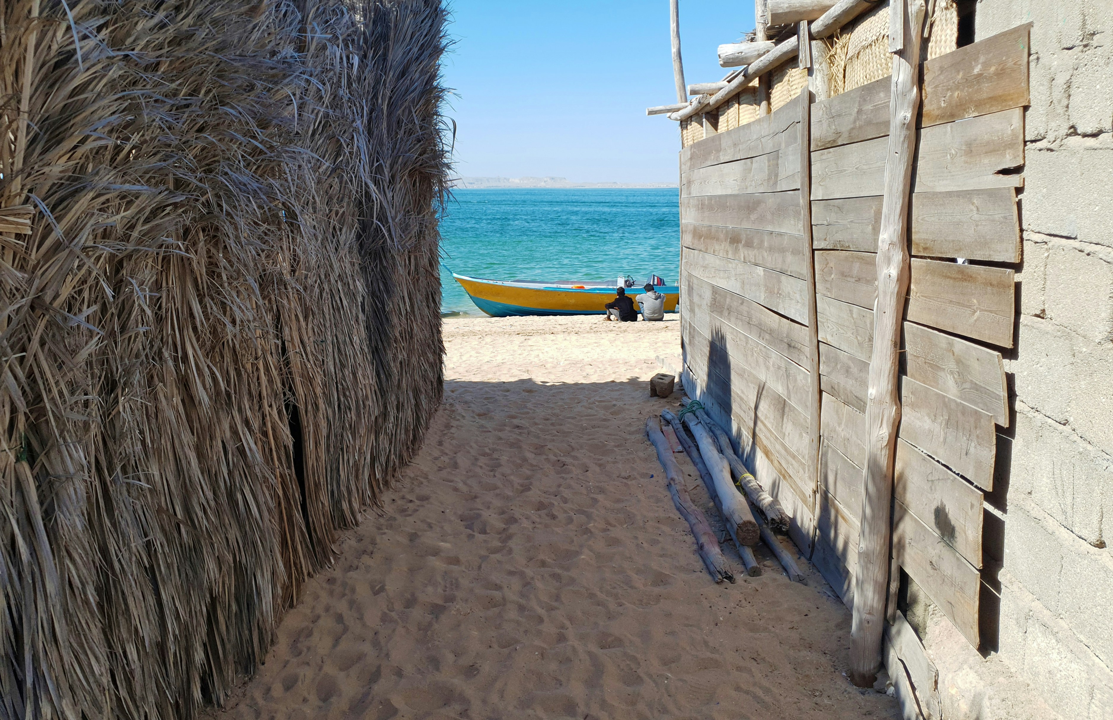 Sandy path between walls leading to a beach and boat.