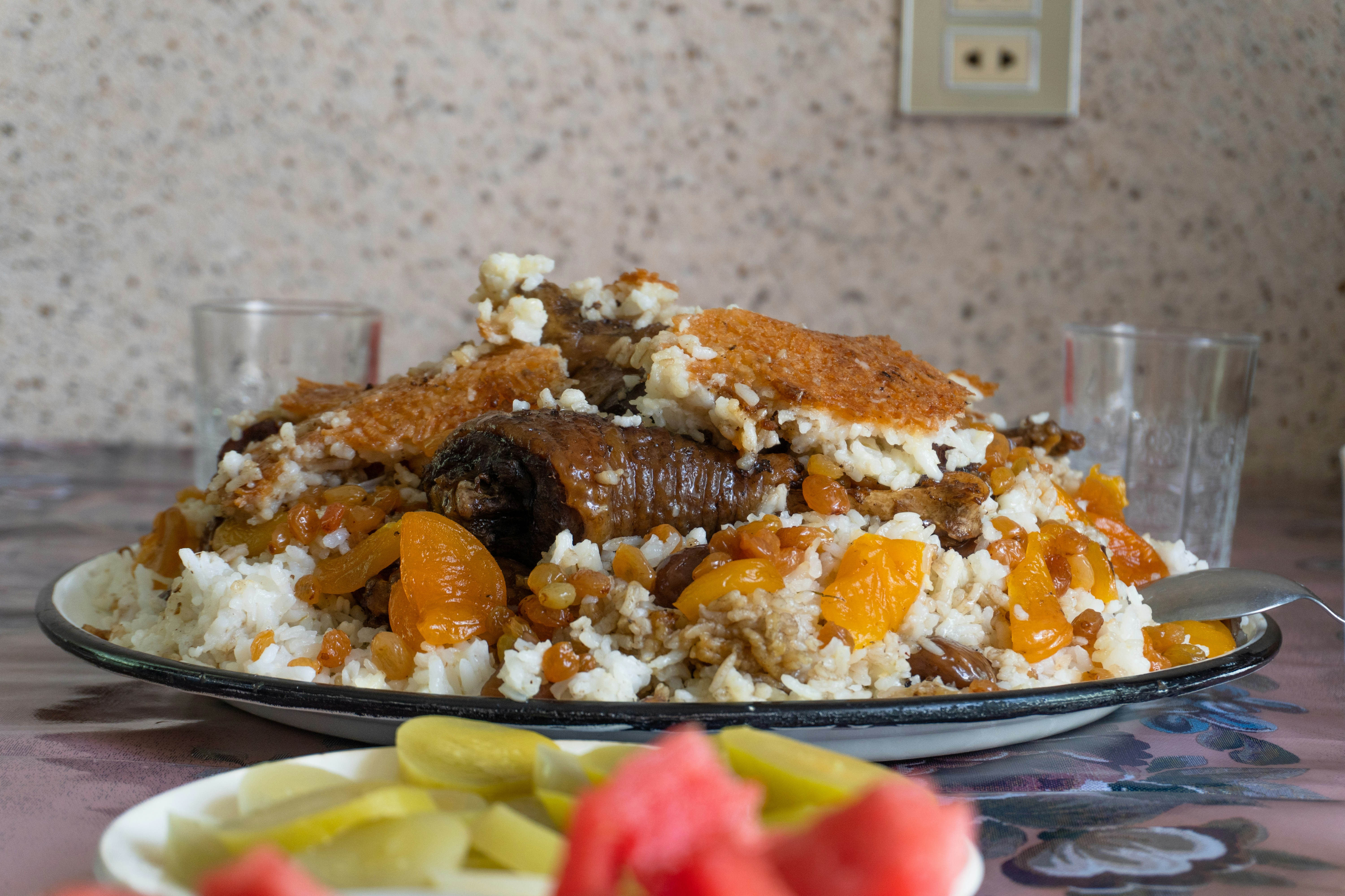 A close-up shot of traditional Azerbaijani chicken plov (pilaf), featuring tender roasted chicken pieces served over a bed of fluffy long-grain rice studded with golden raisins and dried fruit.