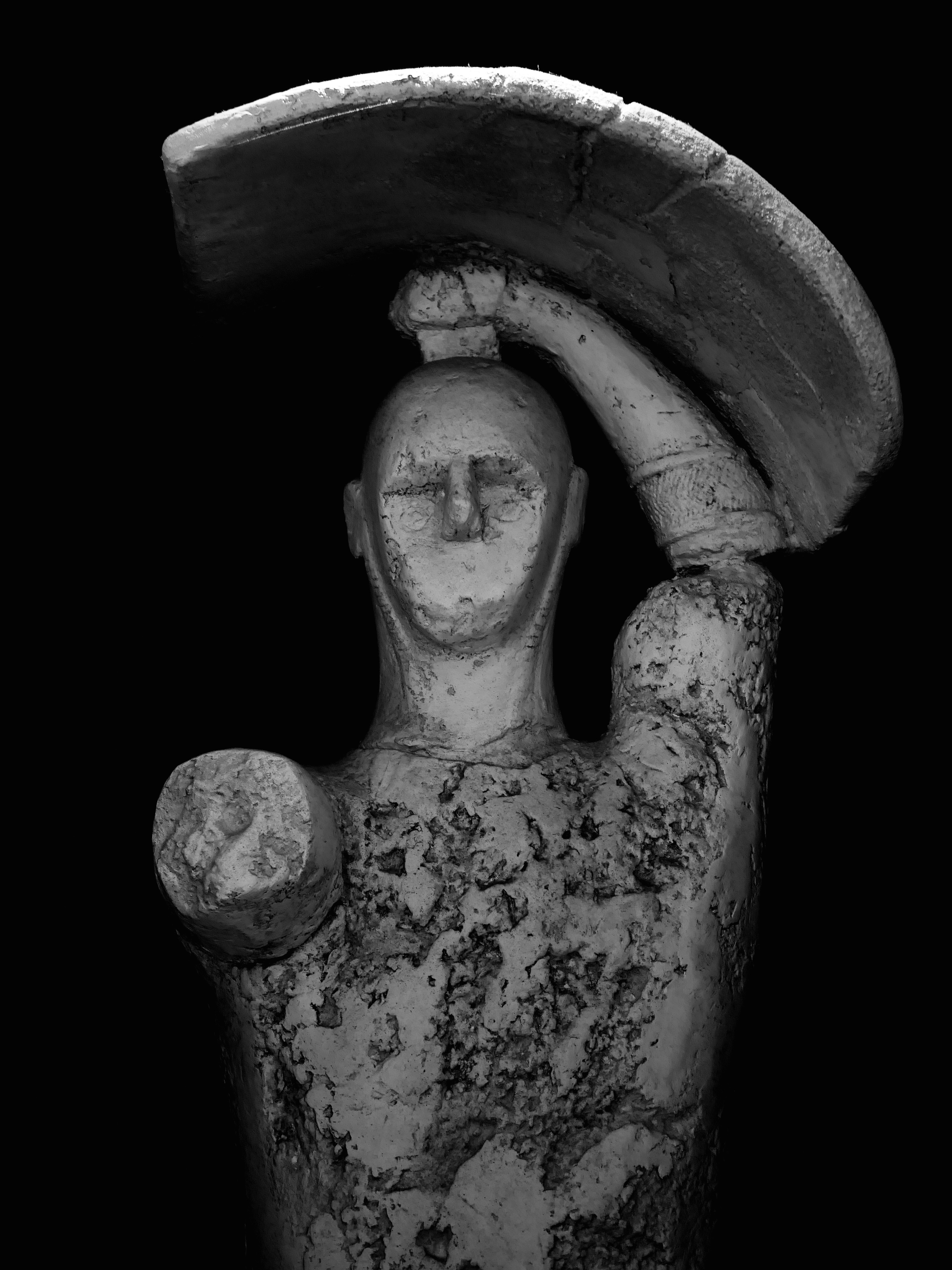 Weathered ancient statue of a figure holding a shield.