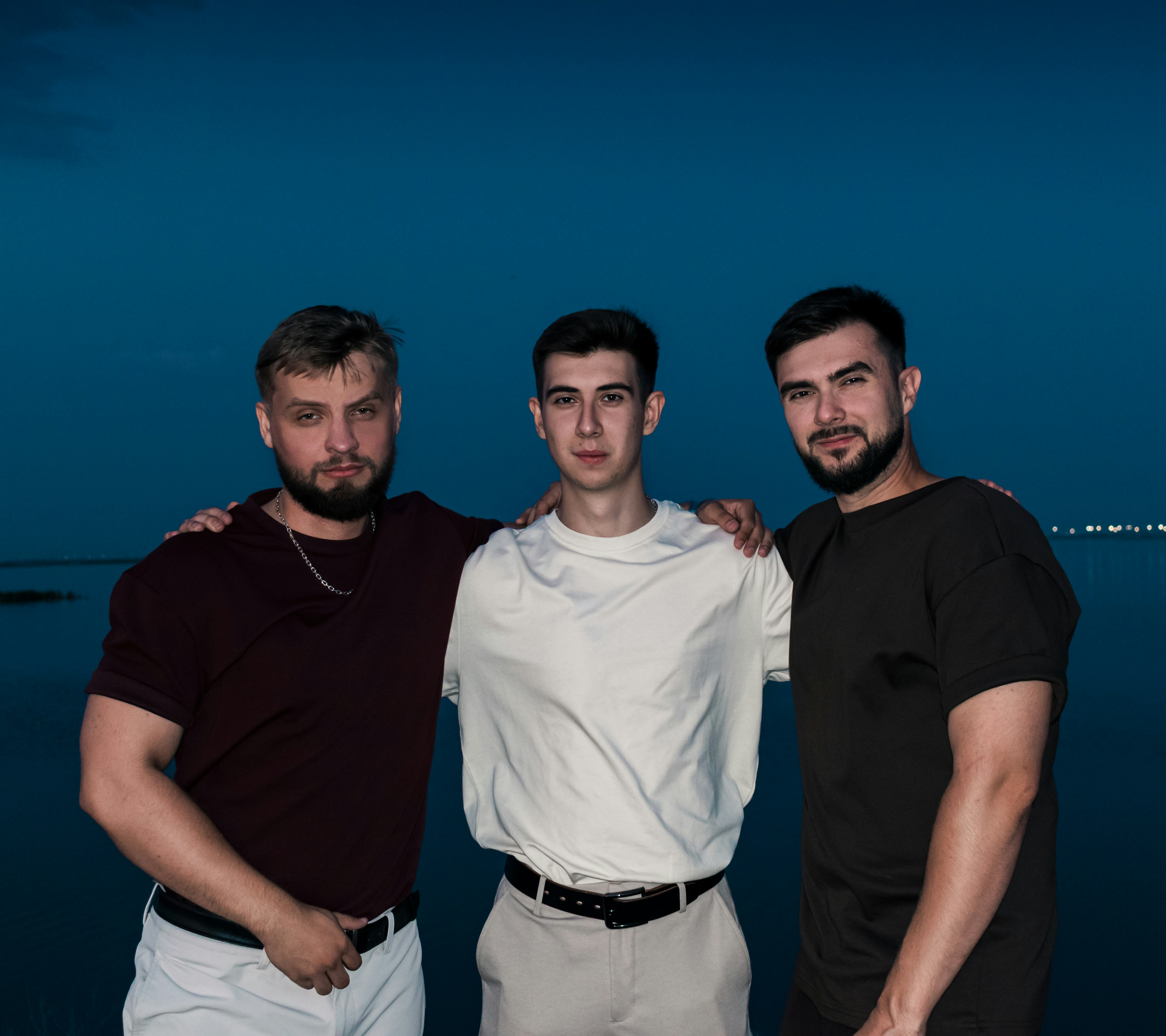 Three men stand together against a dark blue background