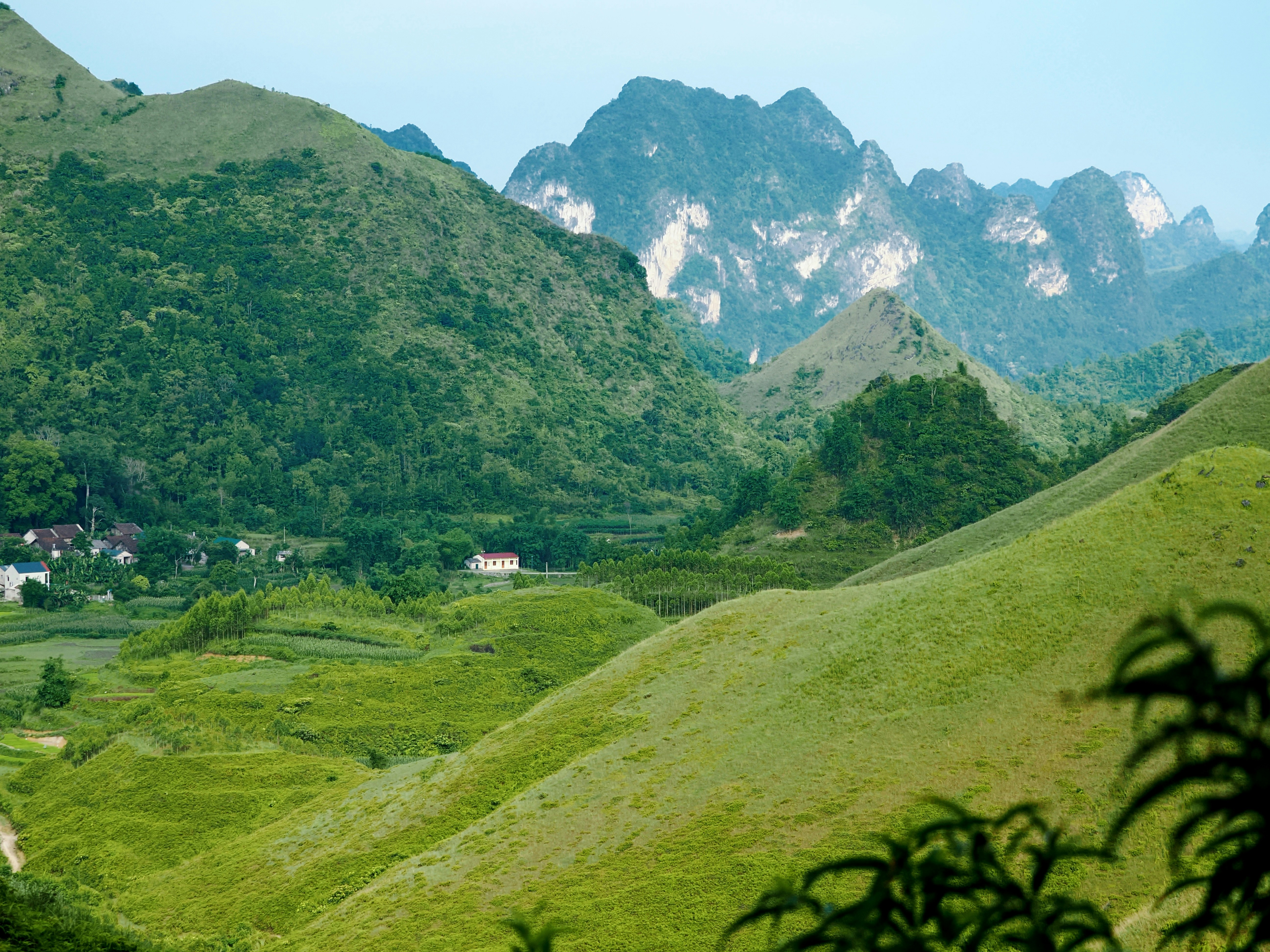 Lush green hills and majestic mountains with a distant village.