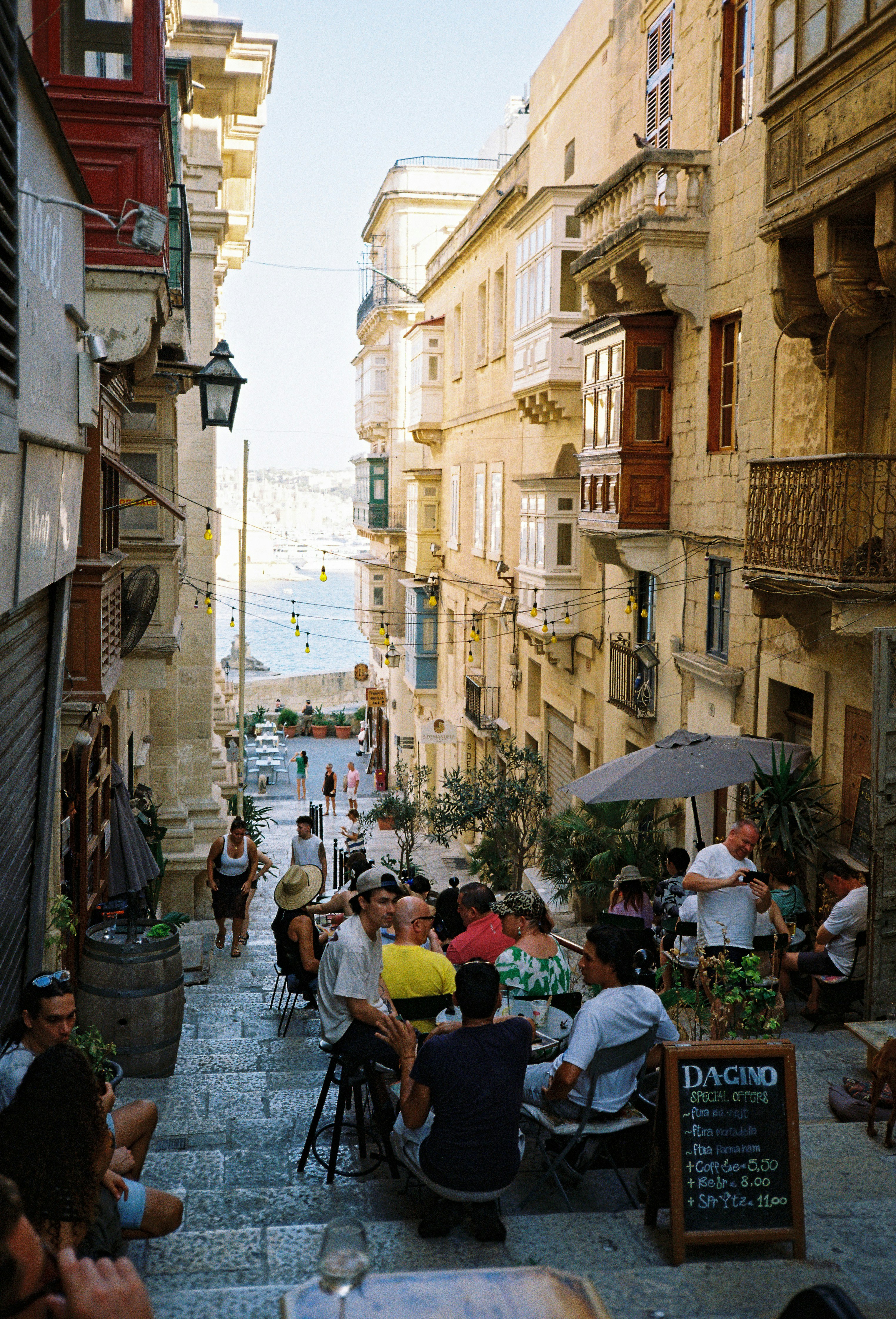 A steep Valletta street lined with cafe tables, leading down to the sea