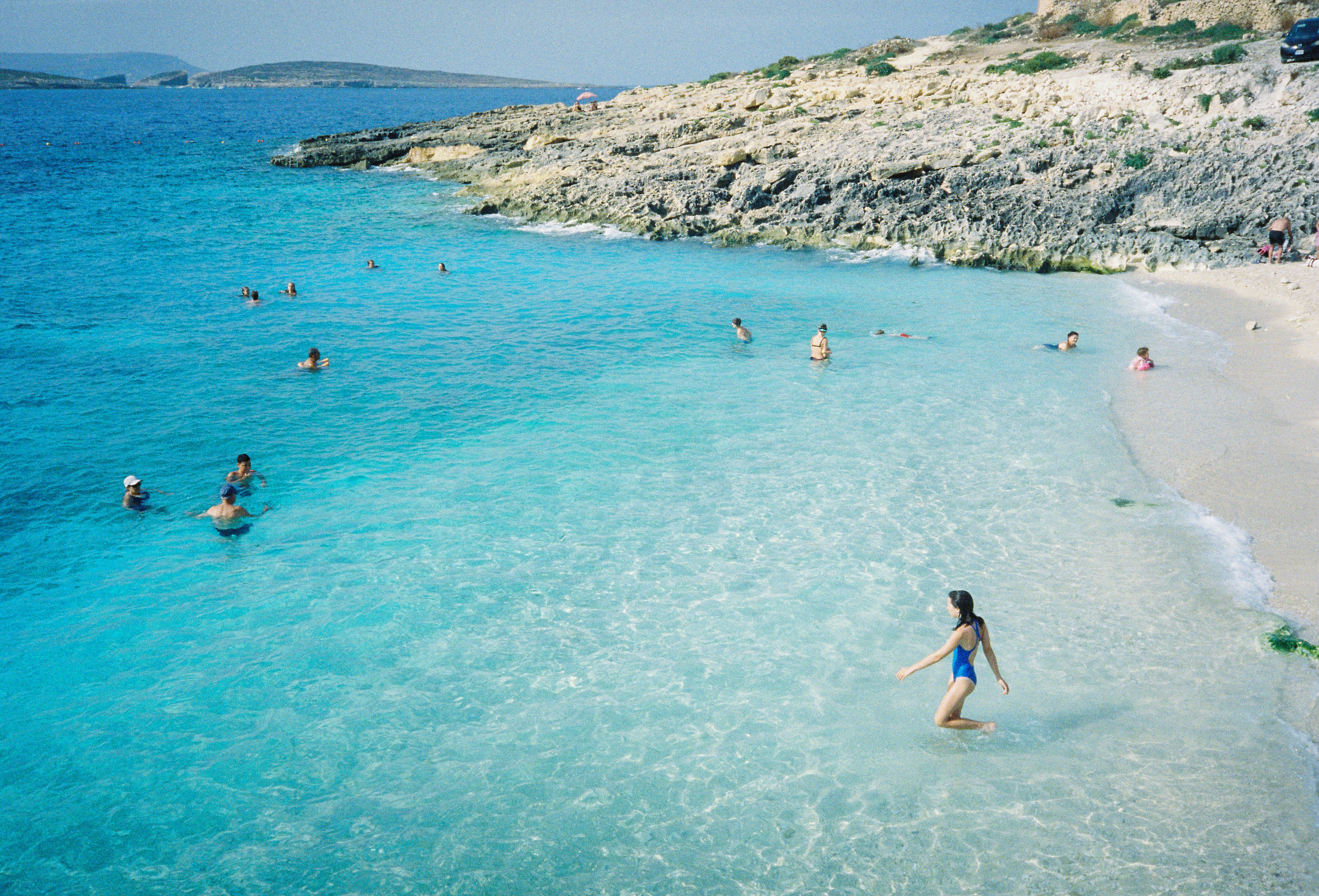 Swimmers enjoying clear turquoise water at a rocky beach