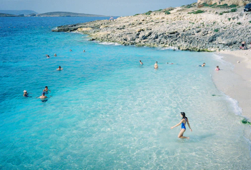 Swimmers enjoying clear turquoise water at a rocky beach