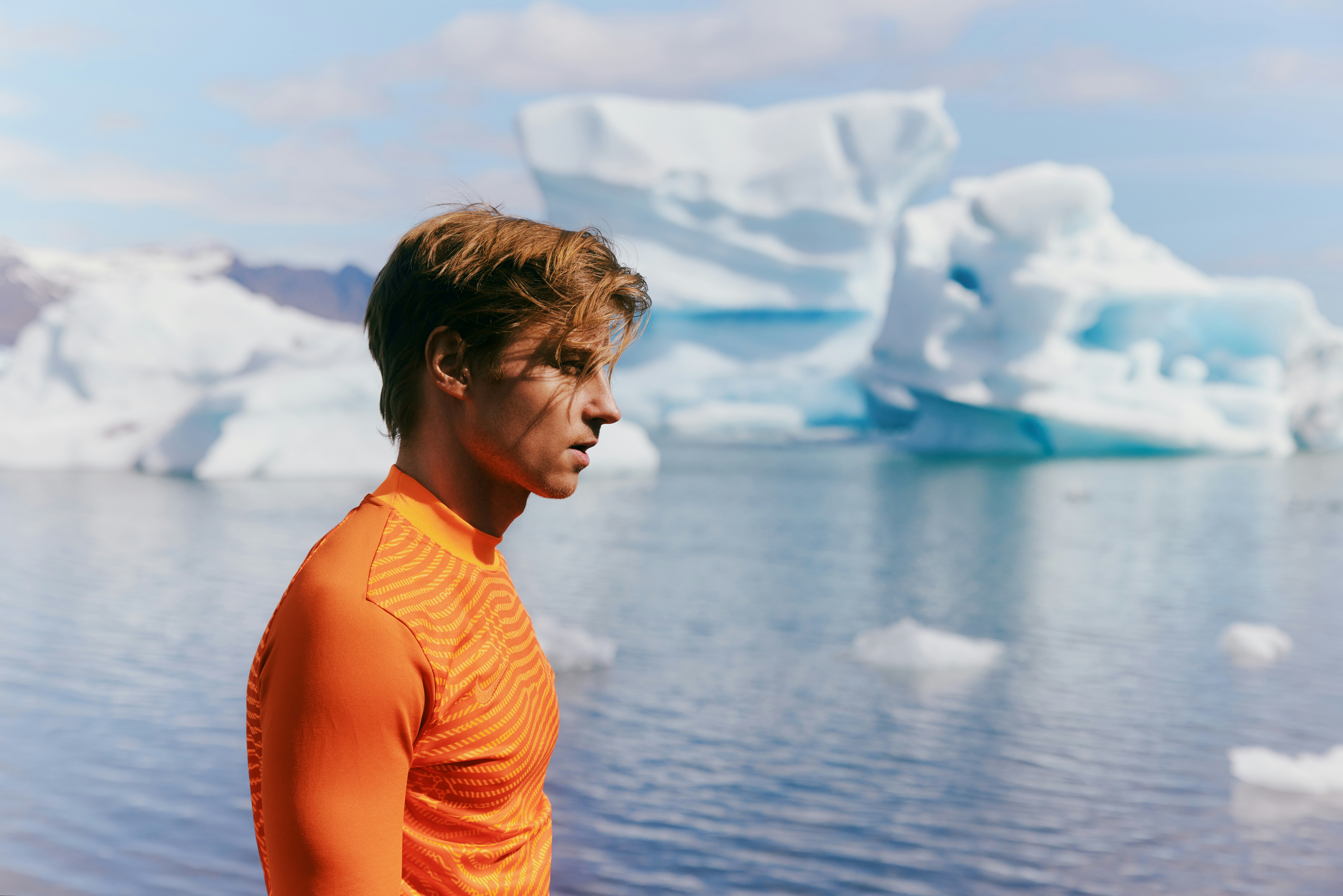 Man in orange shirt by glacial lake with icebergs
