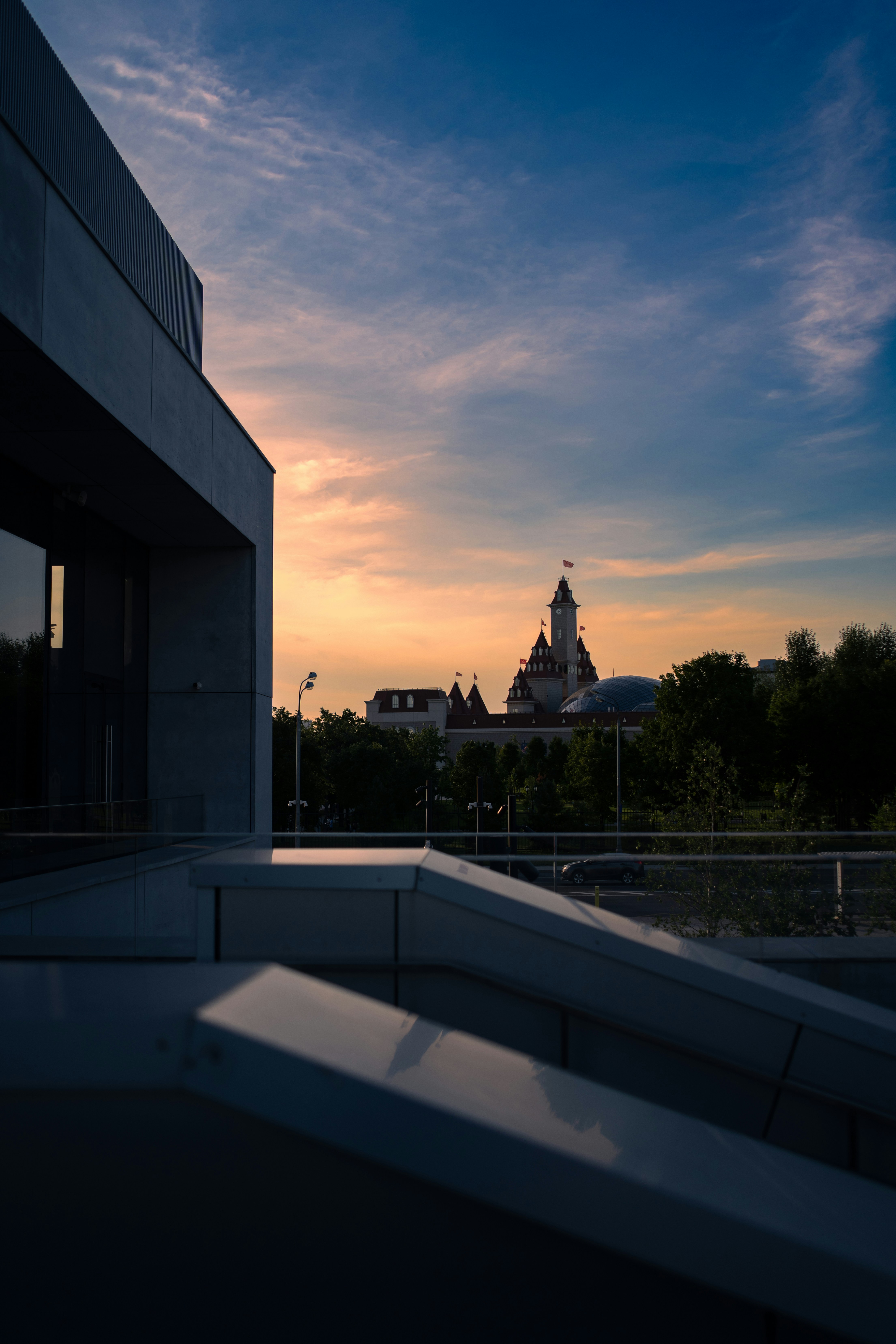 Modern building overlooking a distant castle-like structure at sunset.