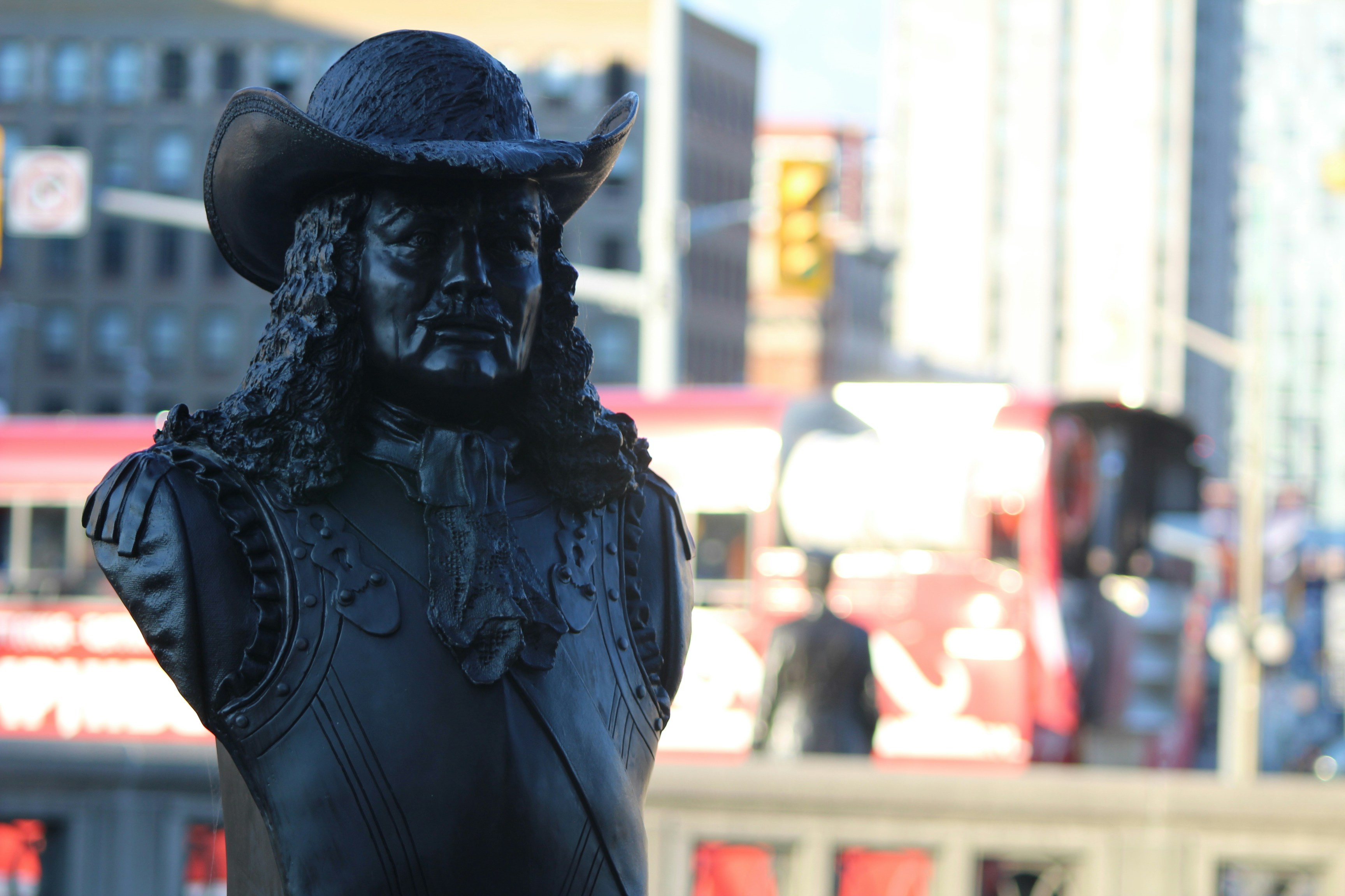 Bronze bust of a man in a hat, city background.
