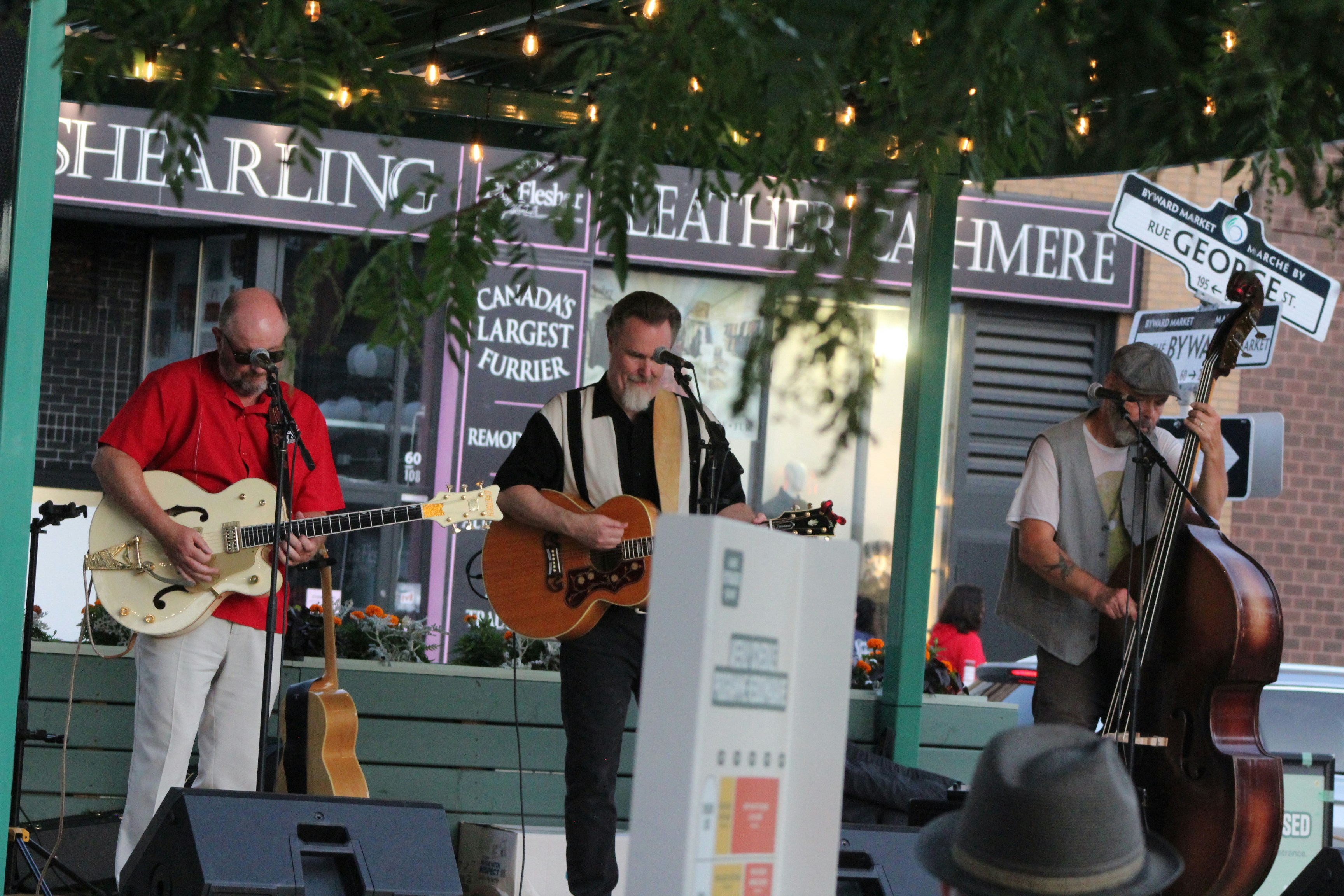 Three musicians perform outdoors with guitars and an upright bass