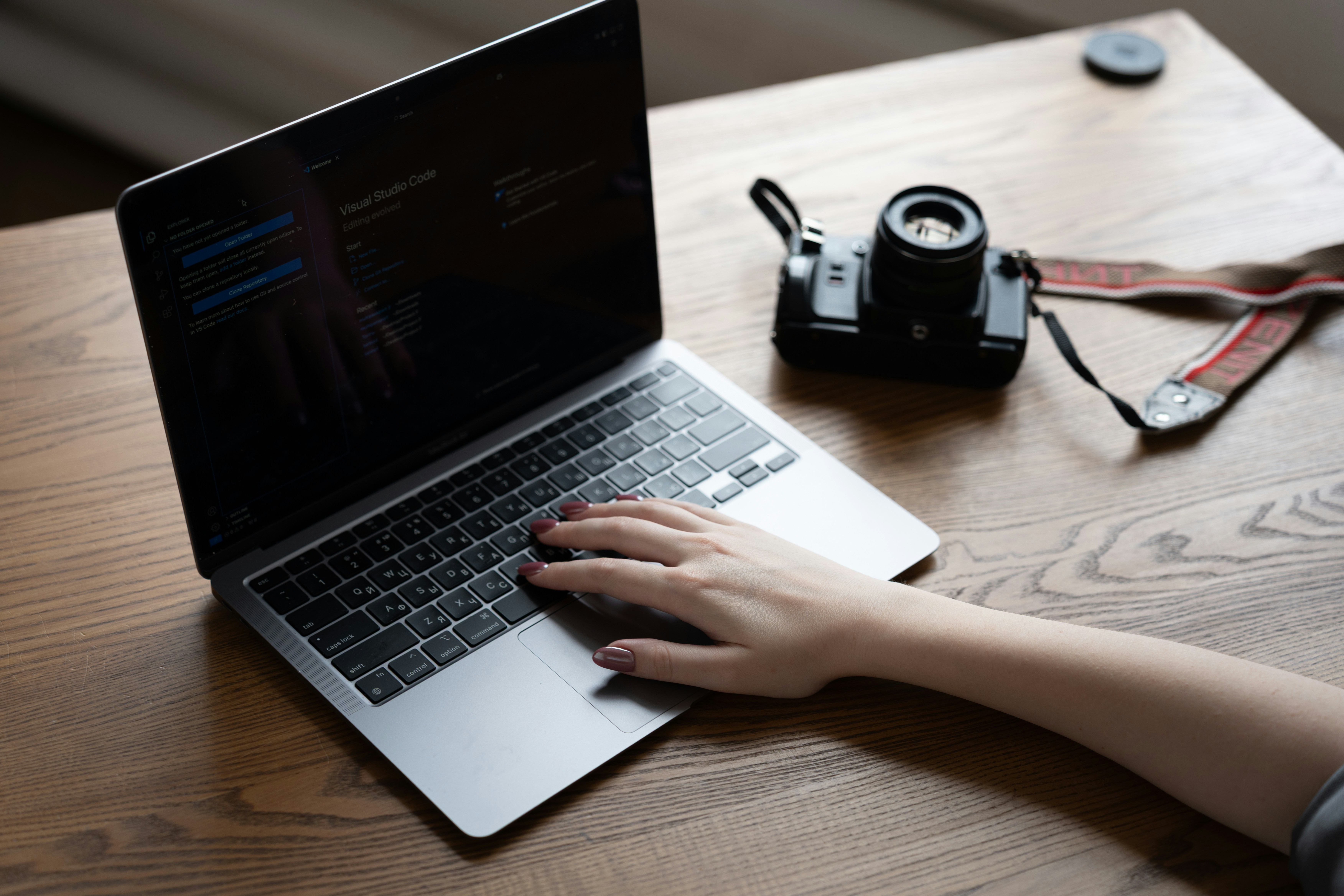 Hand typing on laptop keyboard beside a camera.
