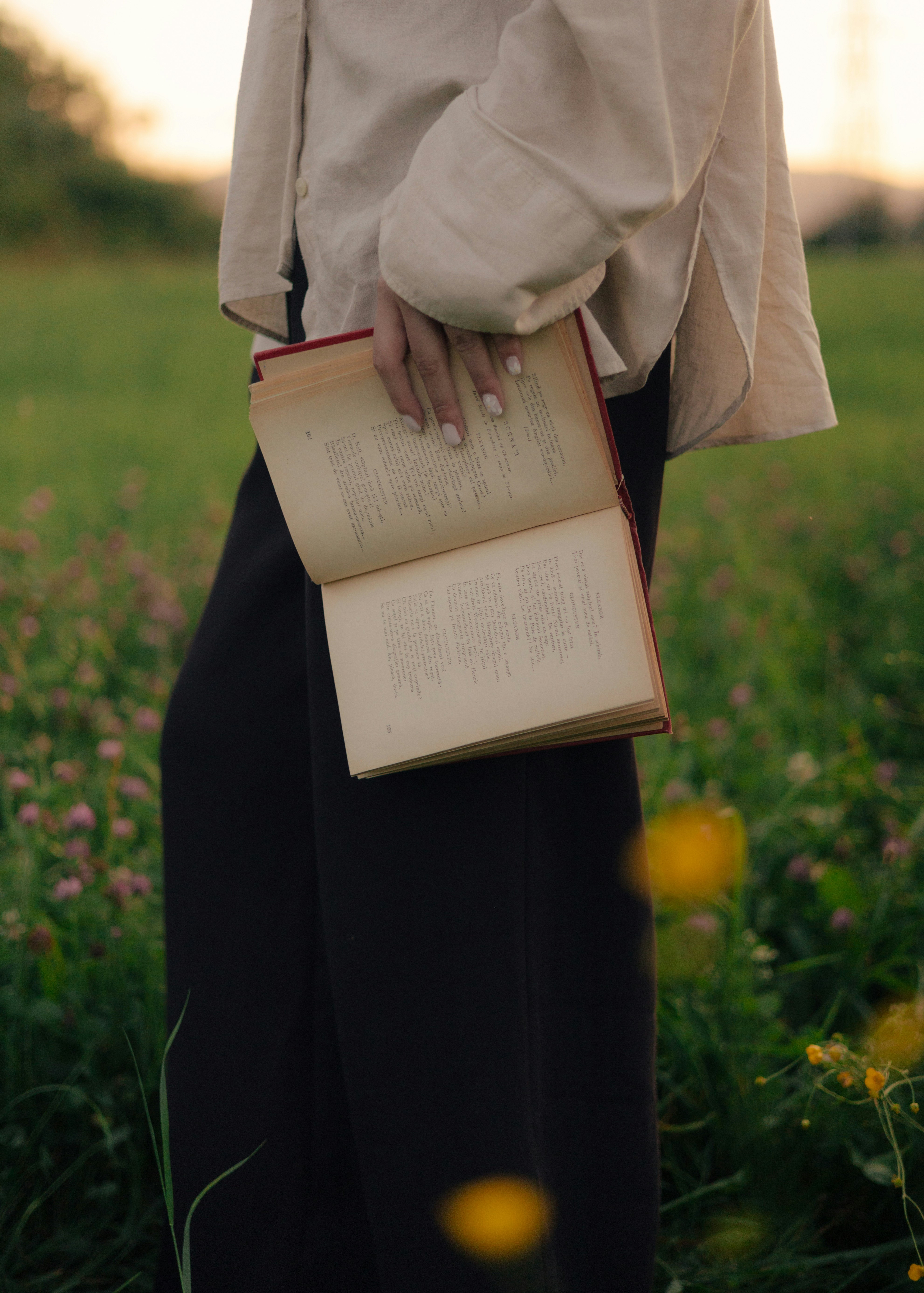 A person holds an open book in a green field