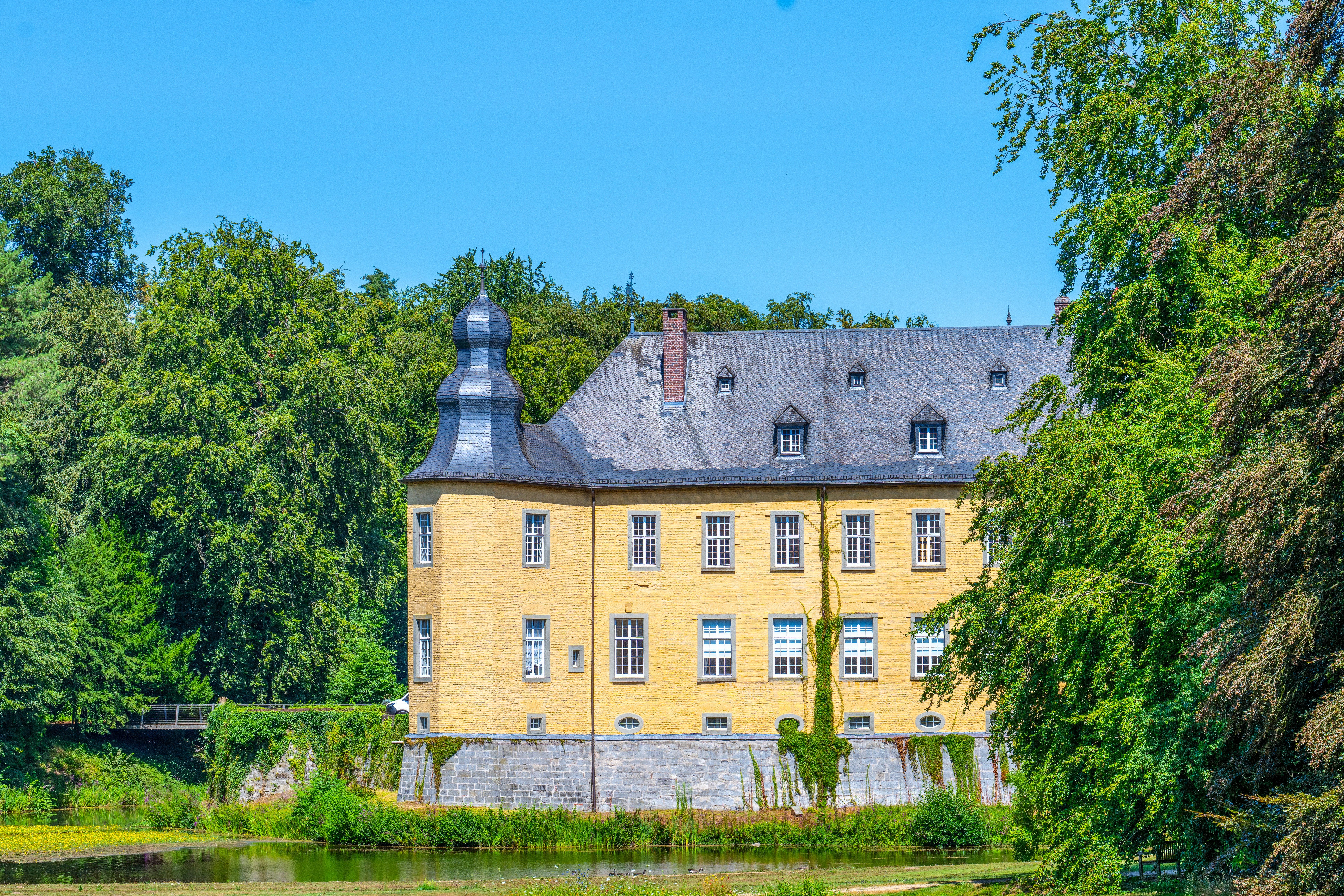Historic yellow castle nestled among trees beside a calm lake.