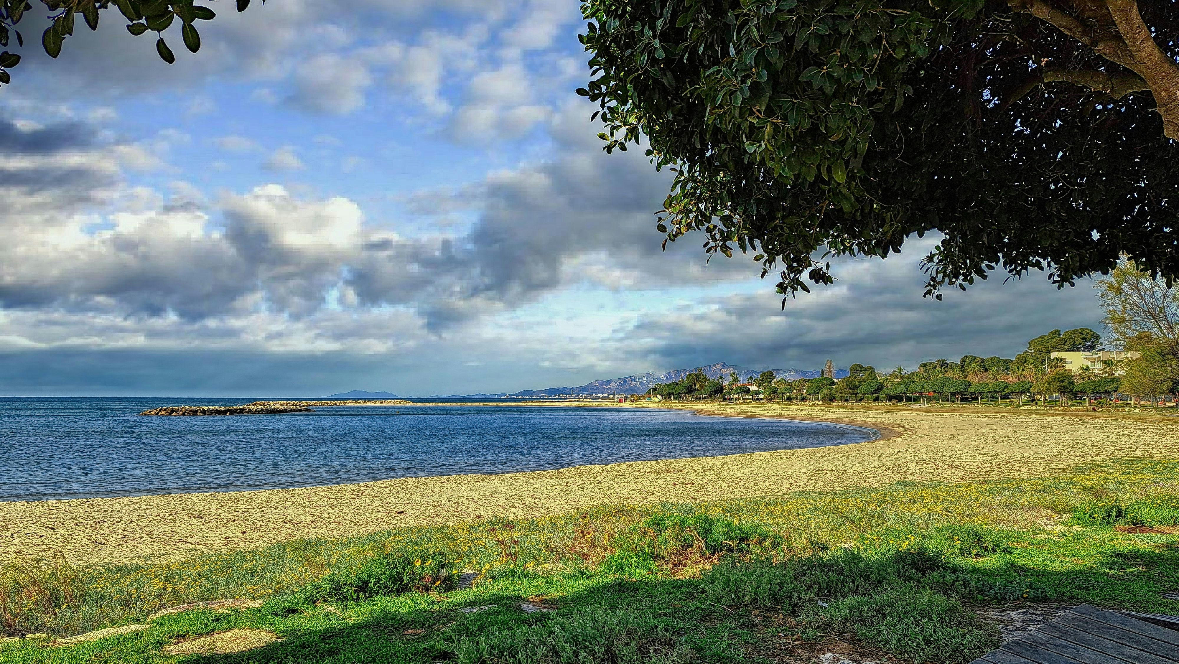 A curved sandy beach and calm ocean under cloudy sky.