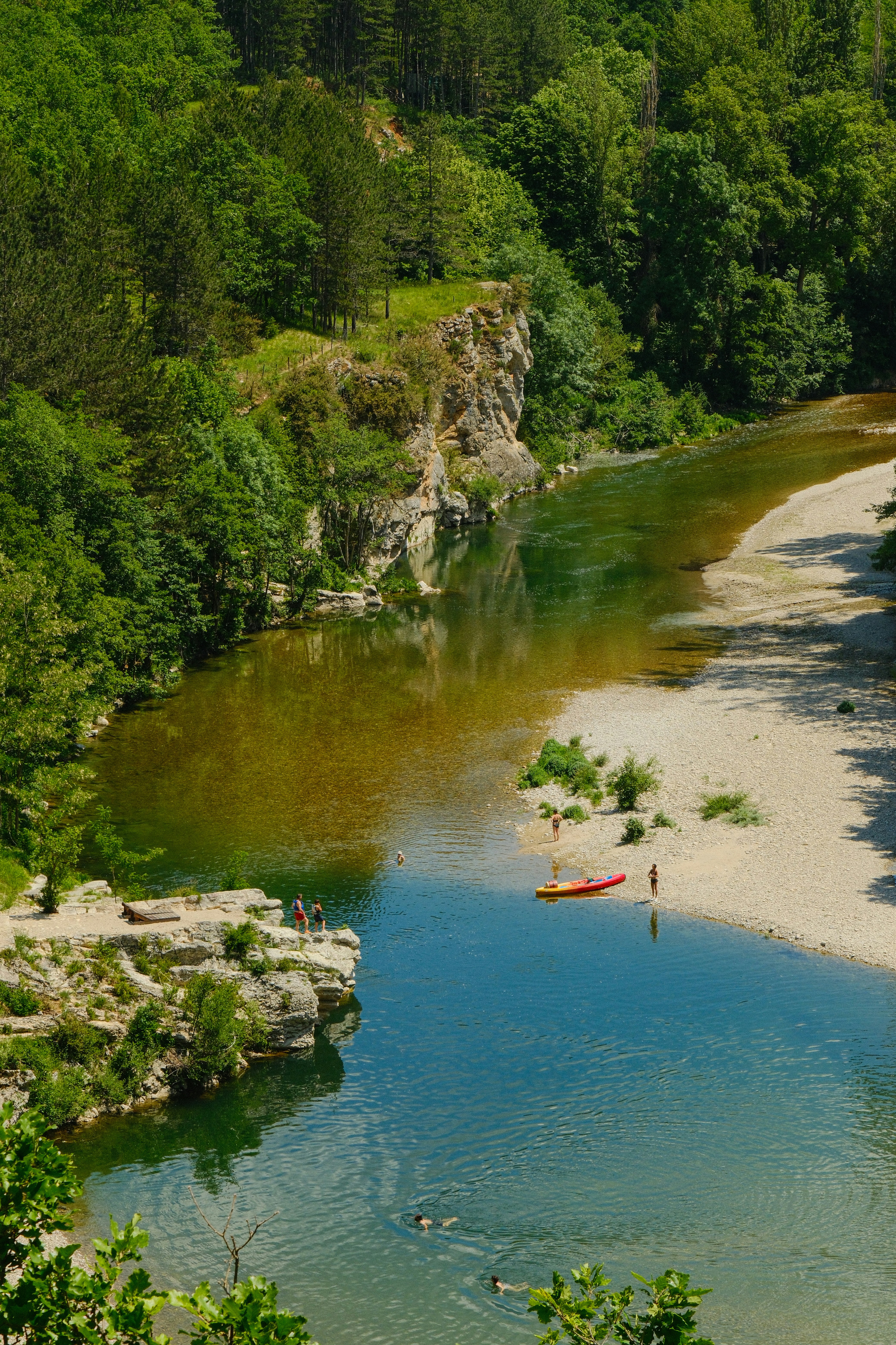 Scenic river flows through forested valley with swimmers and kayak