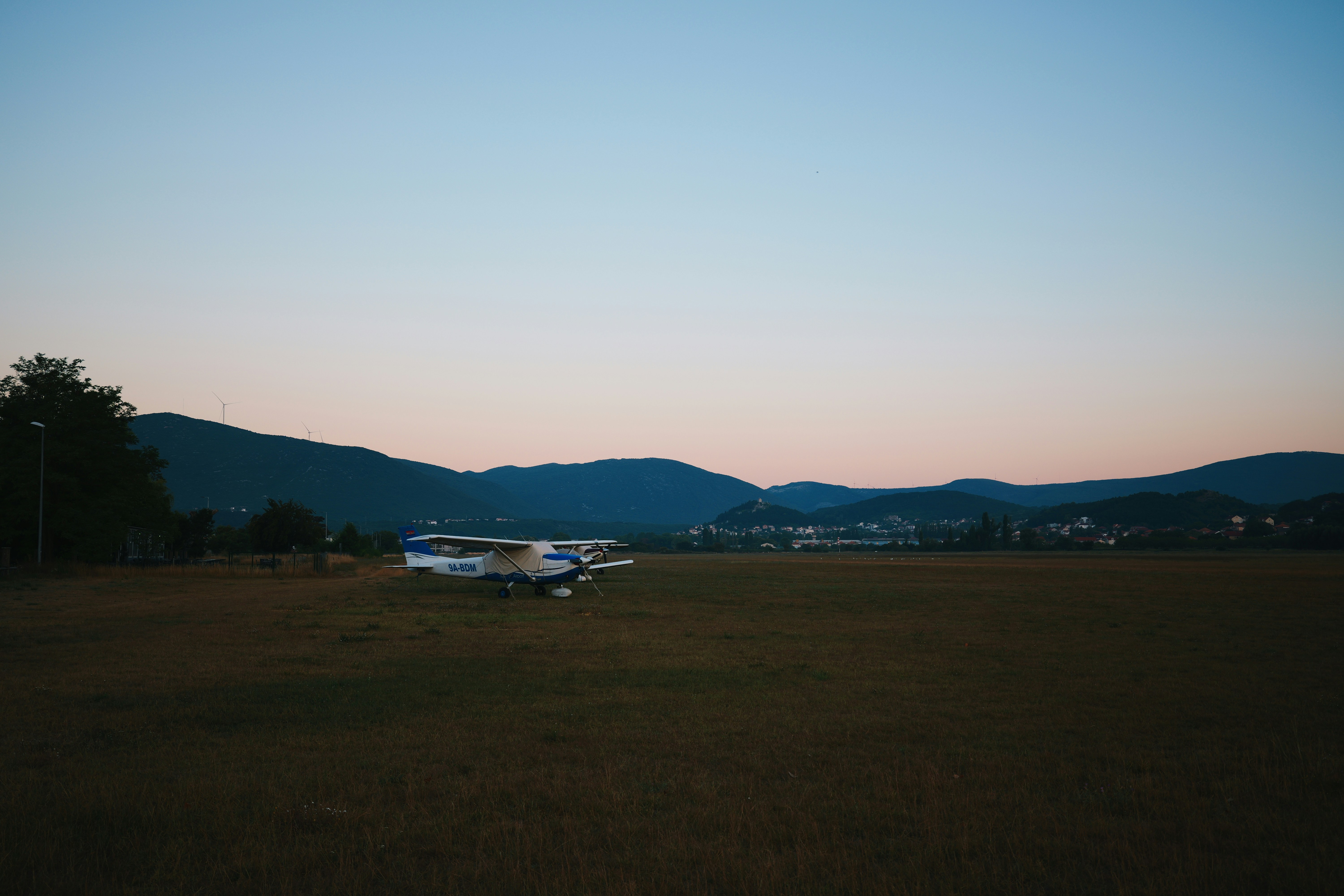 An airplane on a grassy field with mountains at sunset