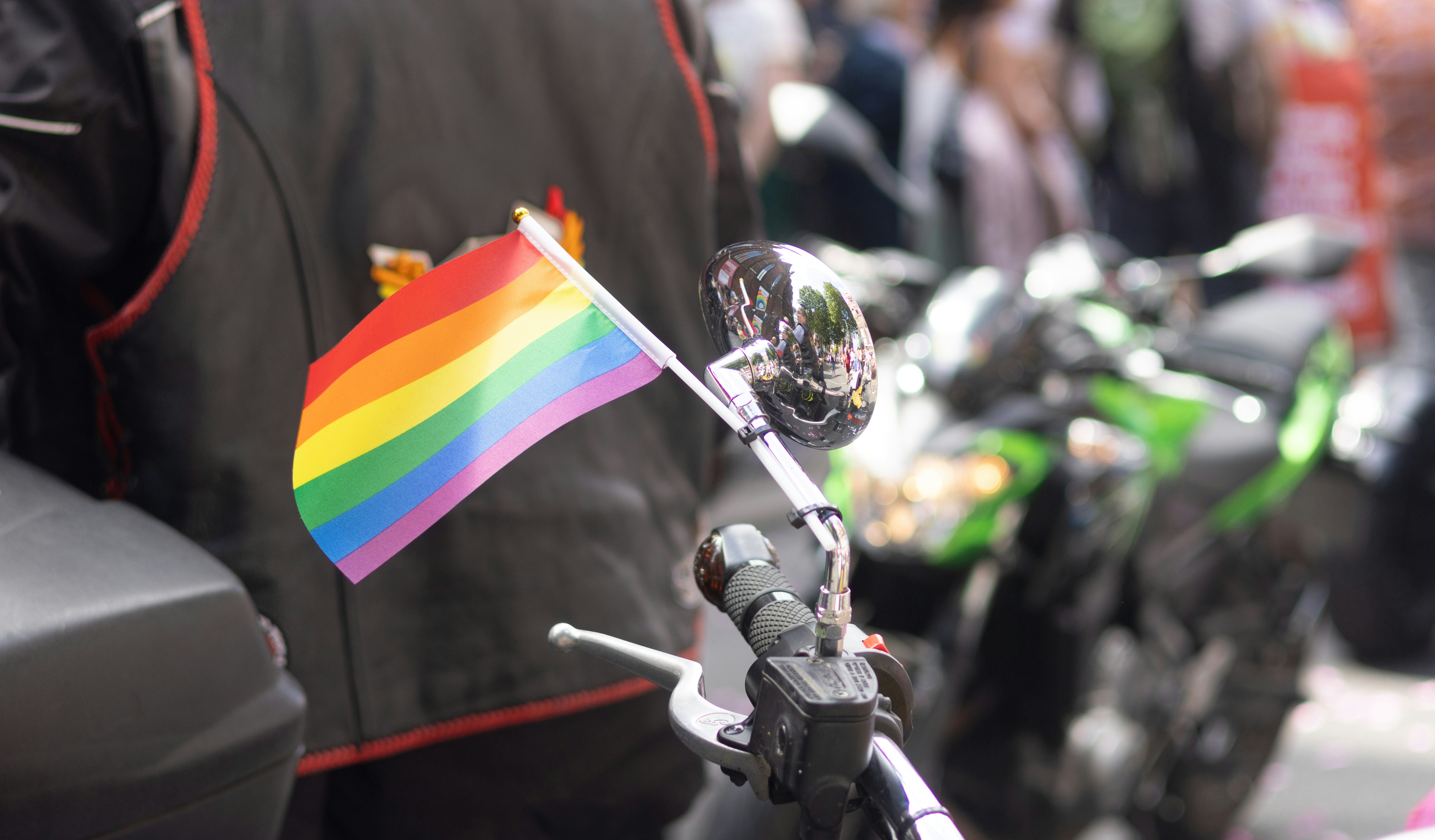 A small rainbow flag attached to a motorcycle handlebar.
