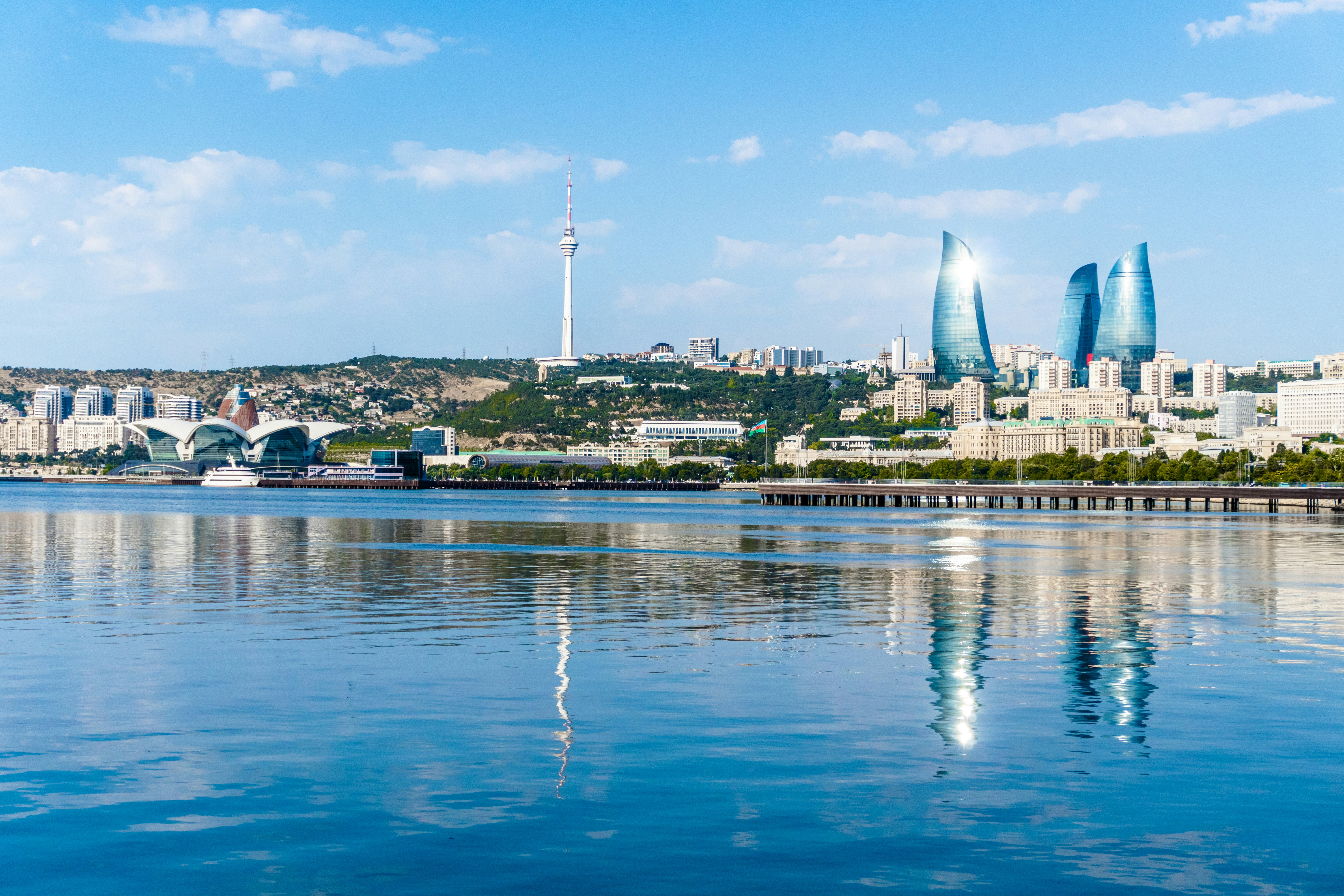 City skyline with modern buildings reflected in calm blue water.