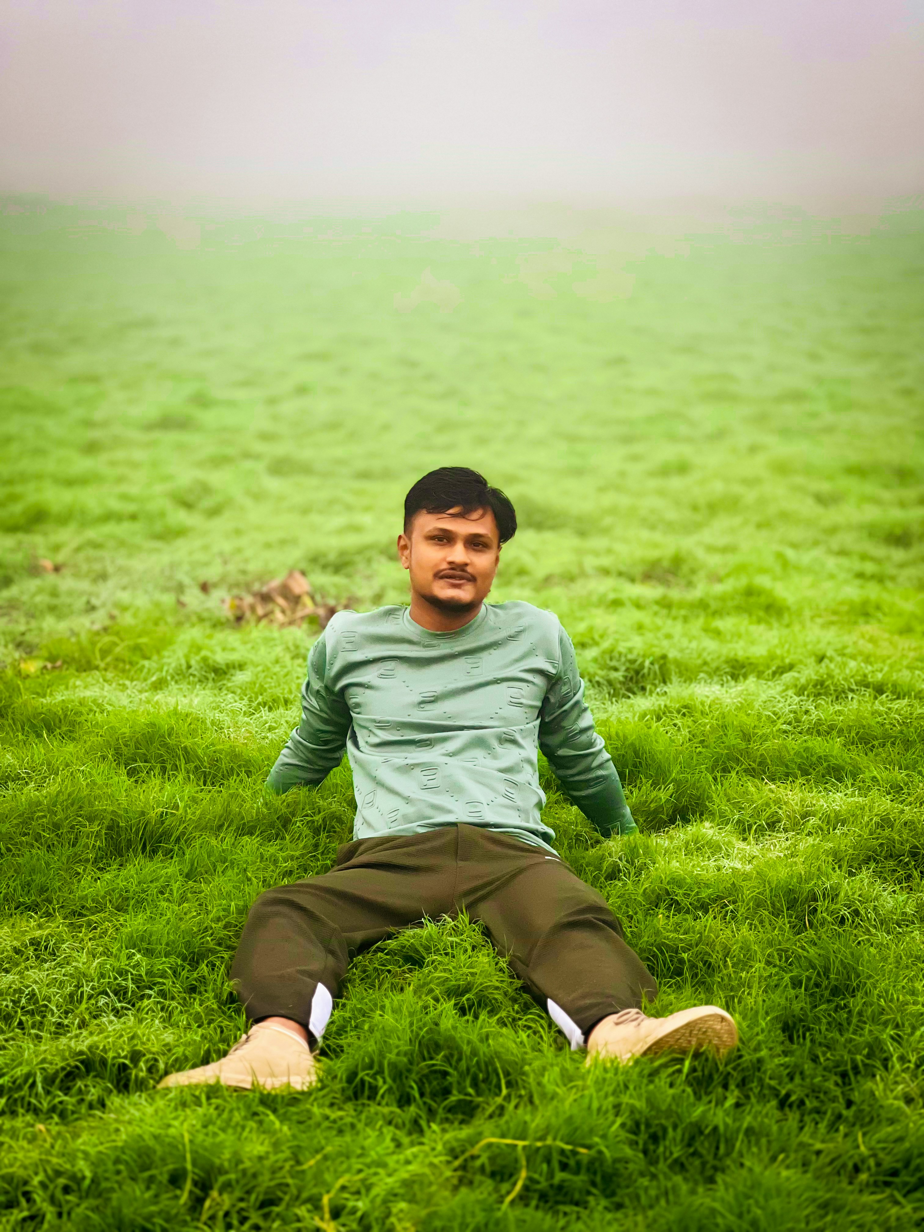Young man sitting in a green field with foggy background