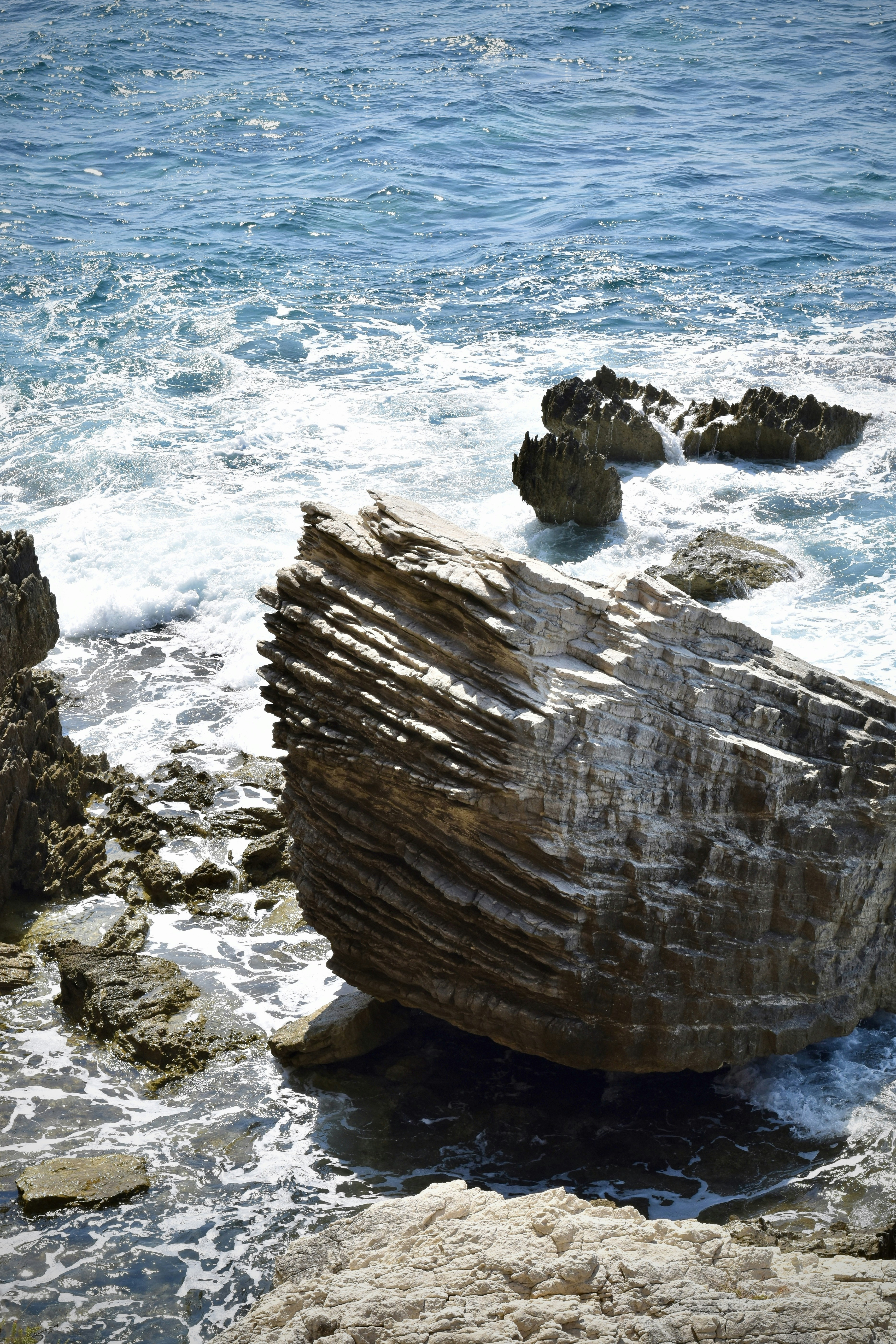 A água azul do oceano envolve uma formação rochosa maciça e em camadas.