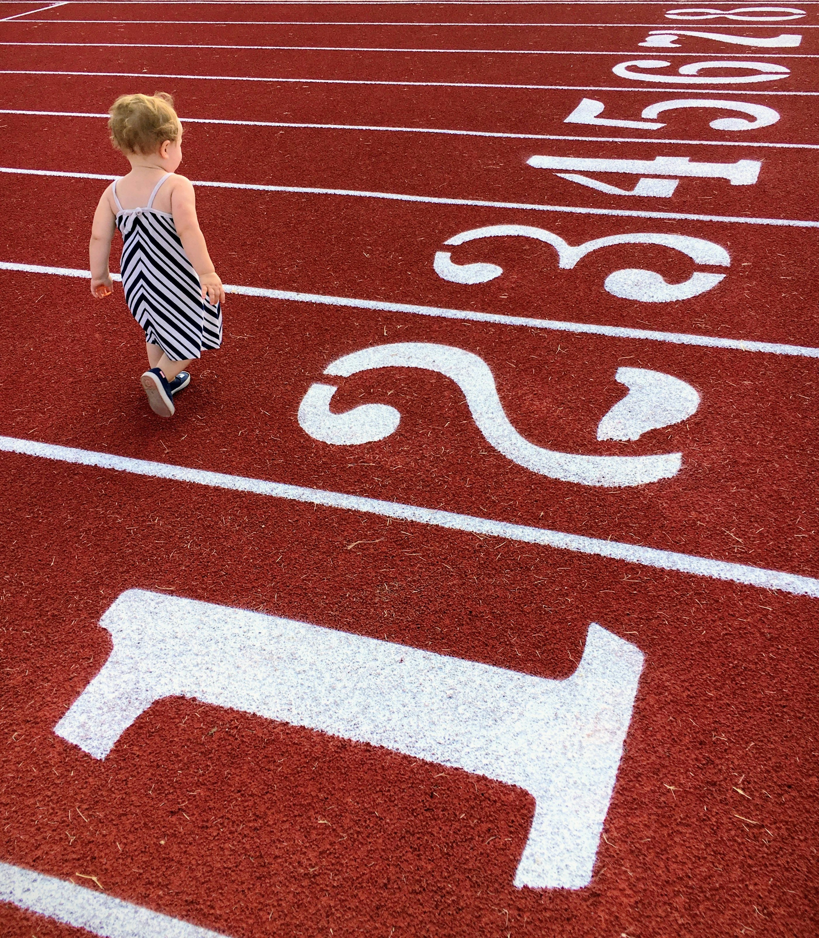 Toddler walking on a red running track with lane numbers