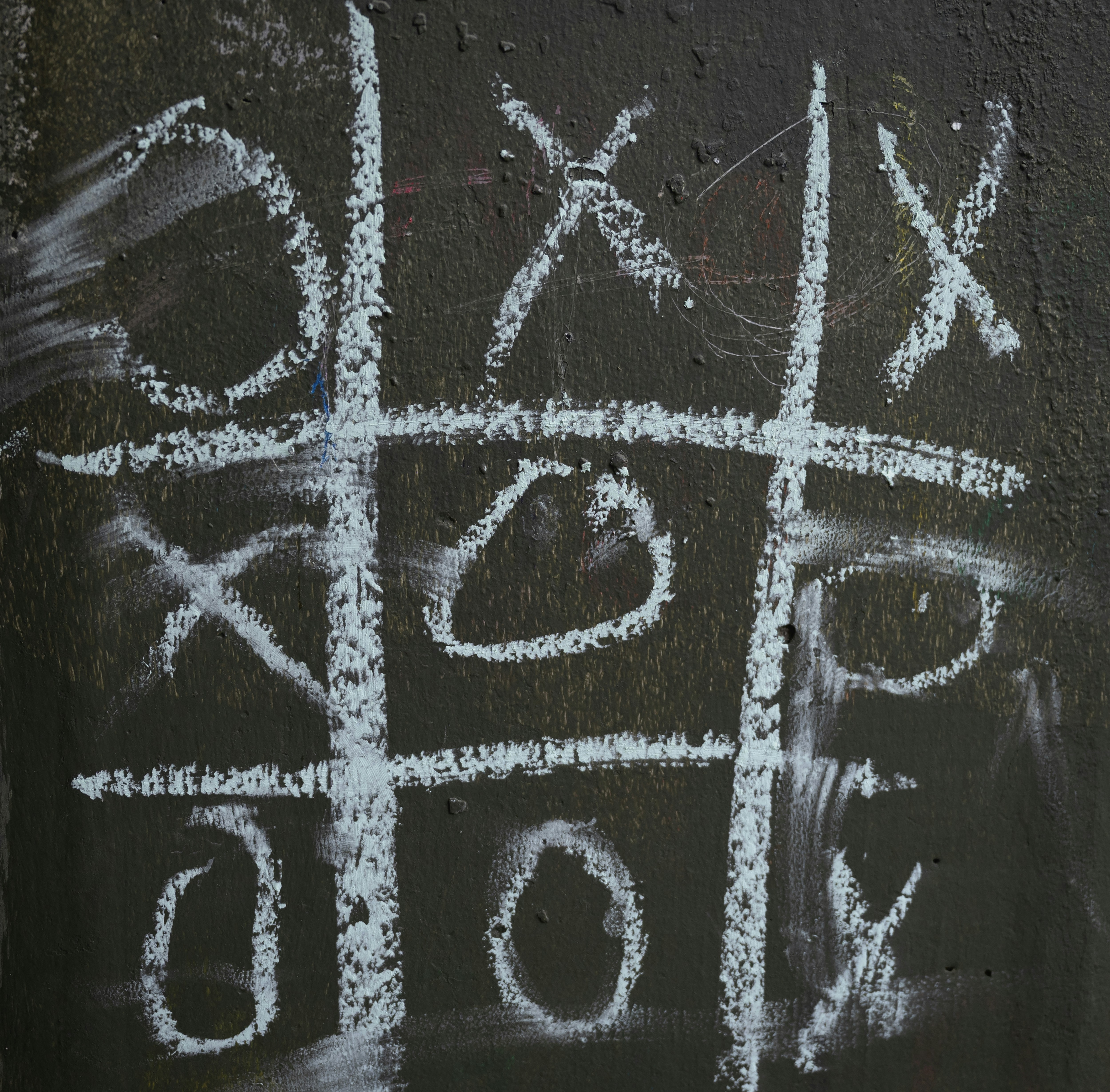 A chalk-drawn tic-tac-toe game on a dark surface.