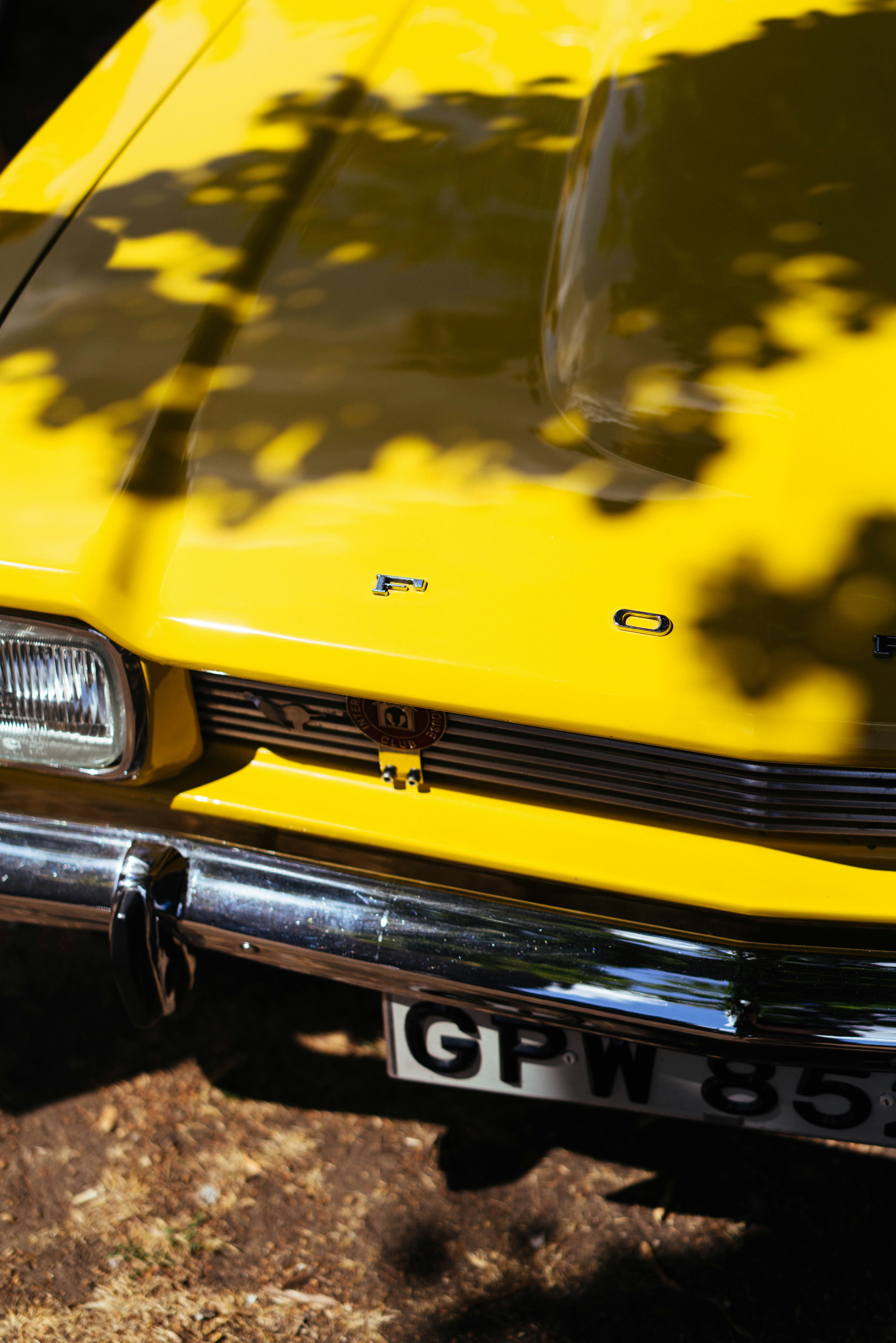 Bright yellow ford car with tree shadows.