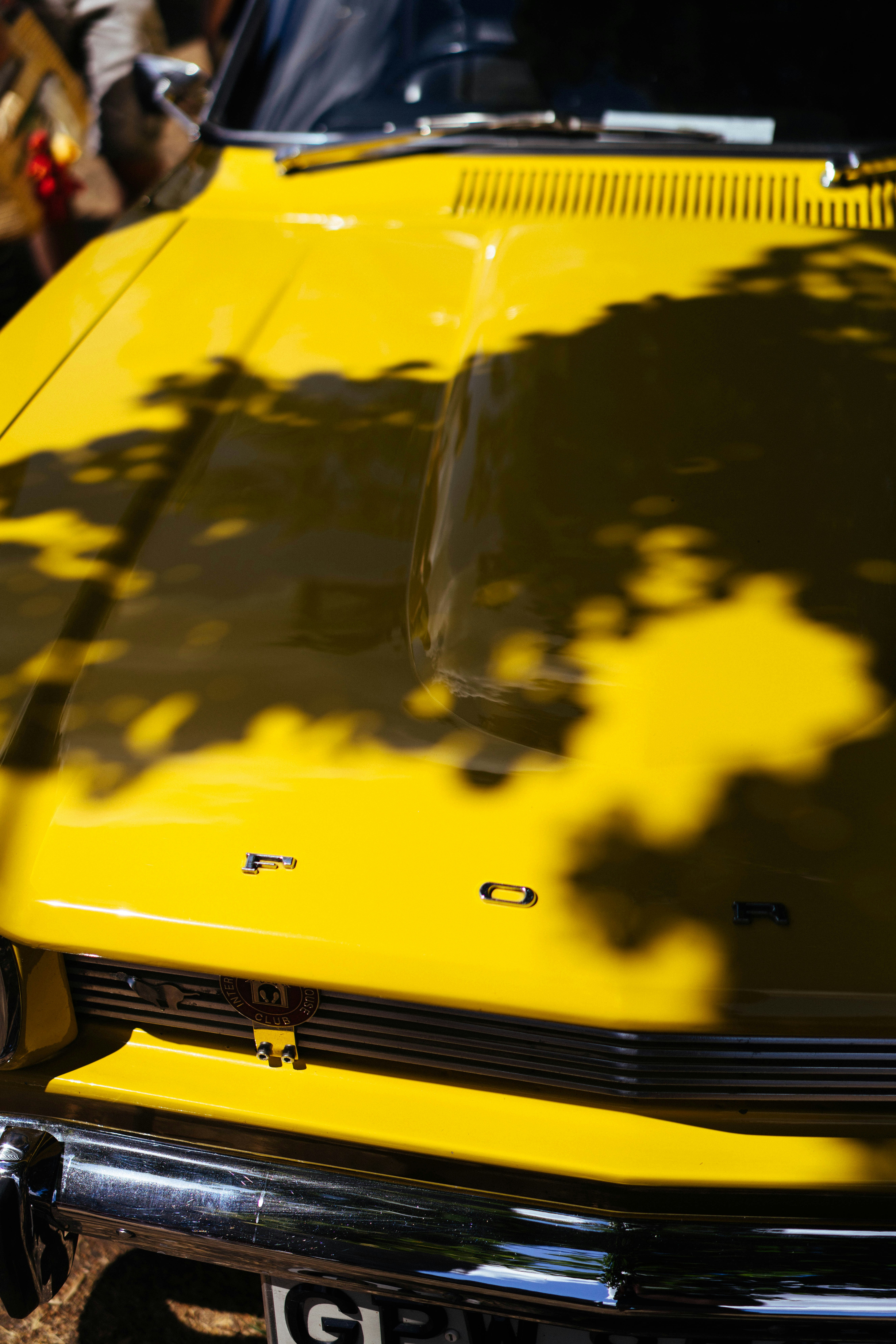 A bright yellow vintage ford car with leaf shadows.