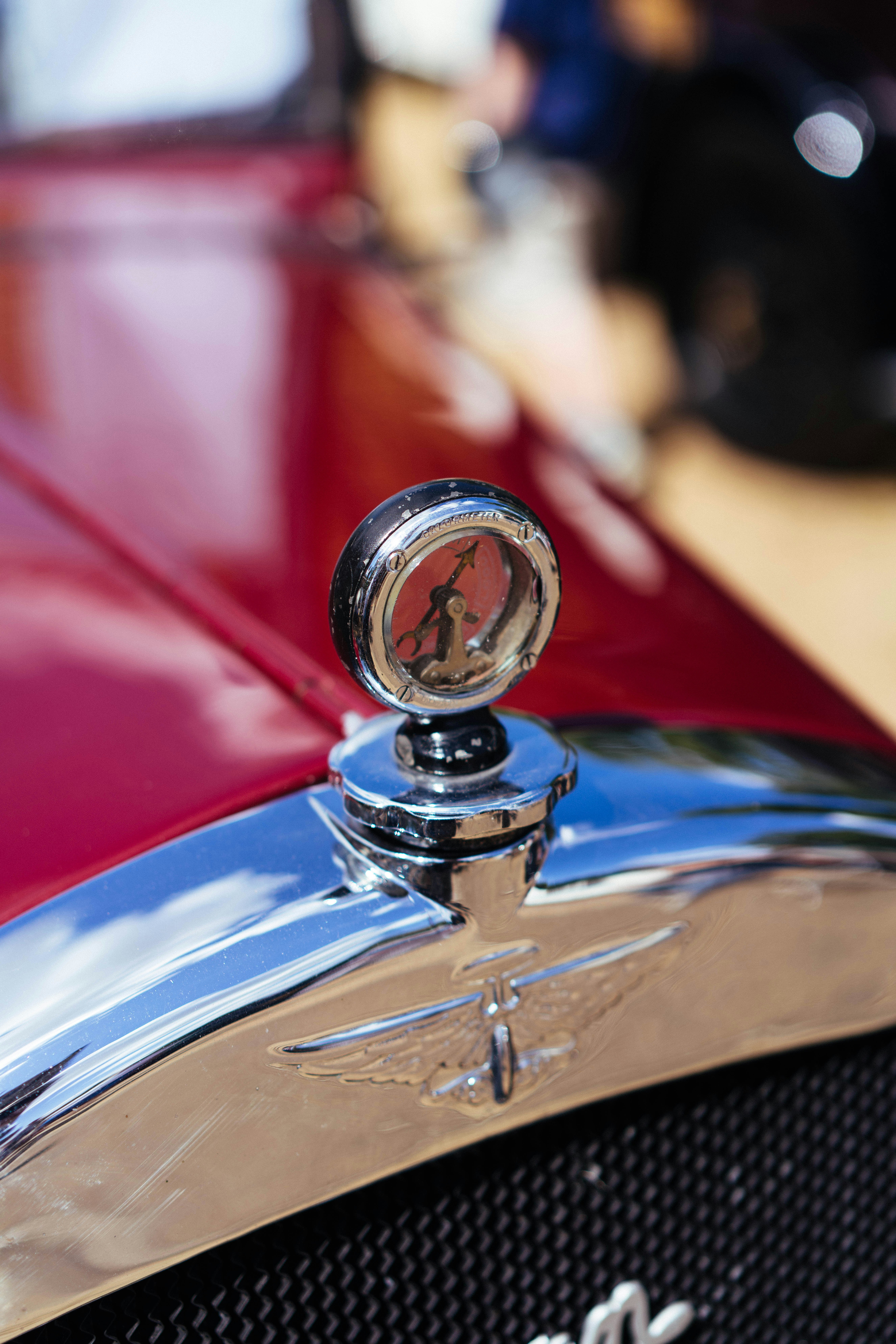 A chrome hood ornament on a vintage red car's grille.