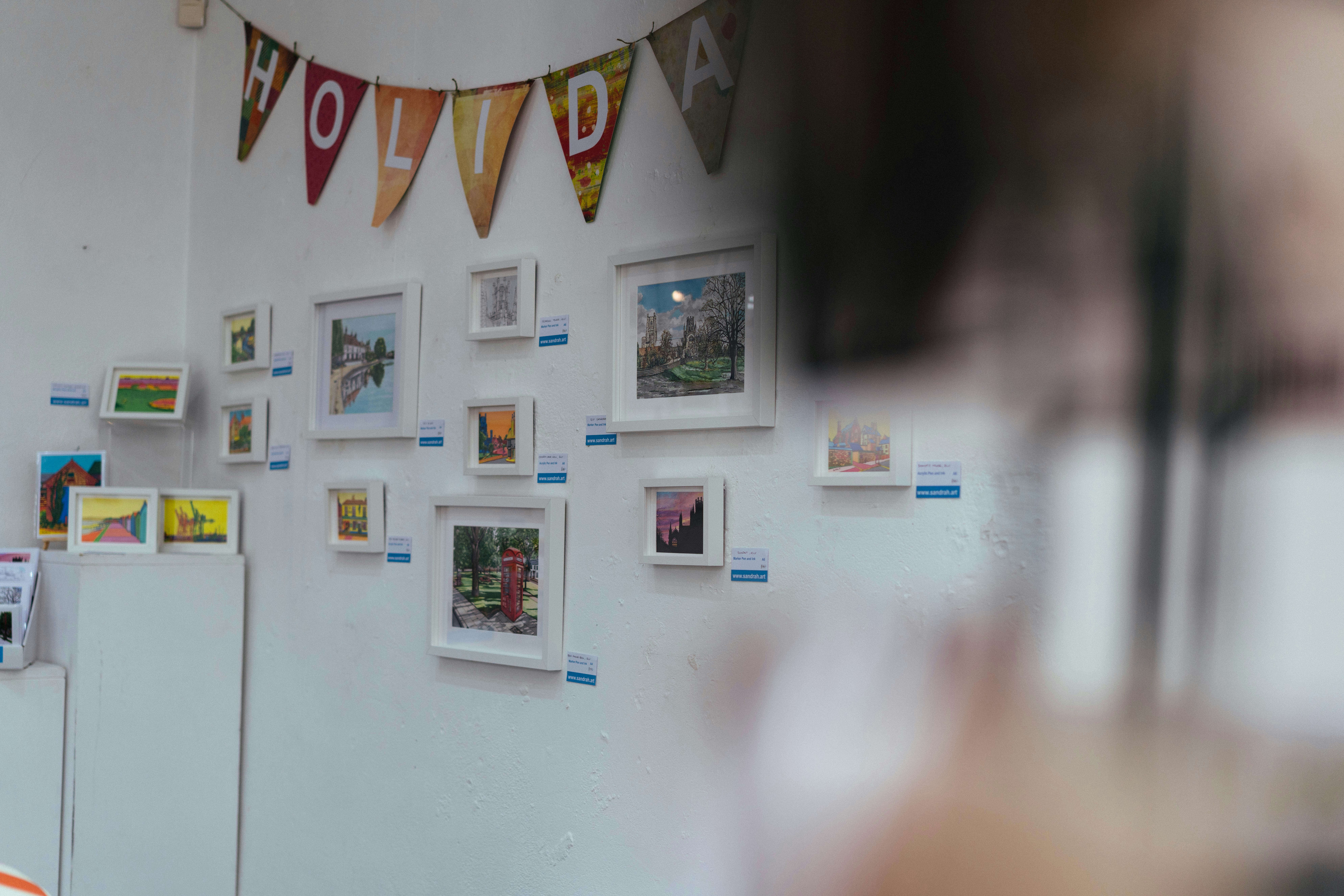 Framed artworks and a 'holiday' banner on a white wall.