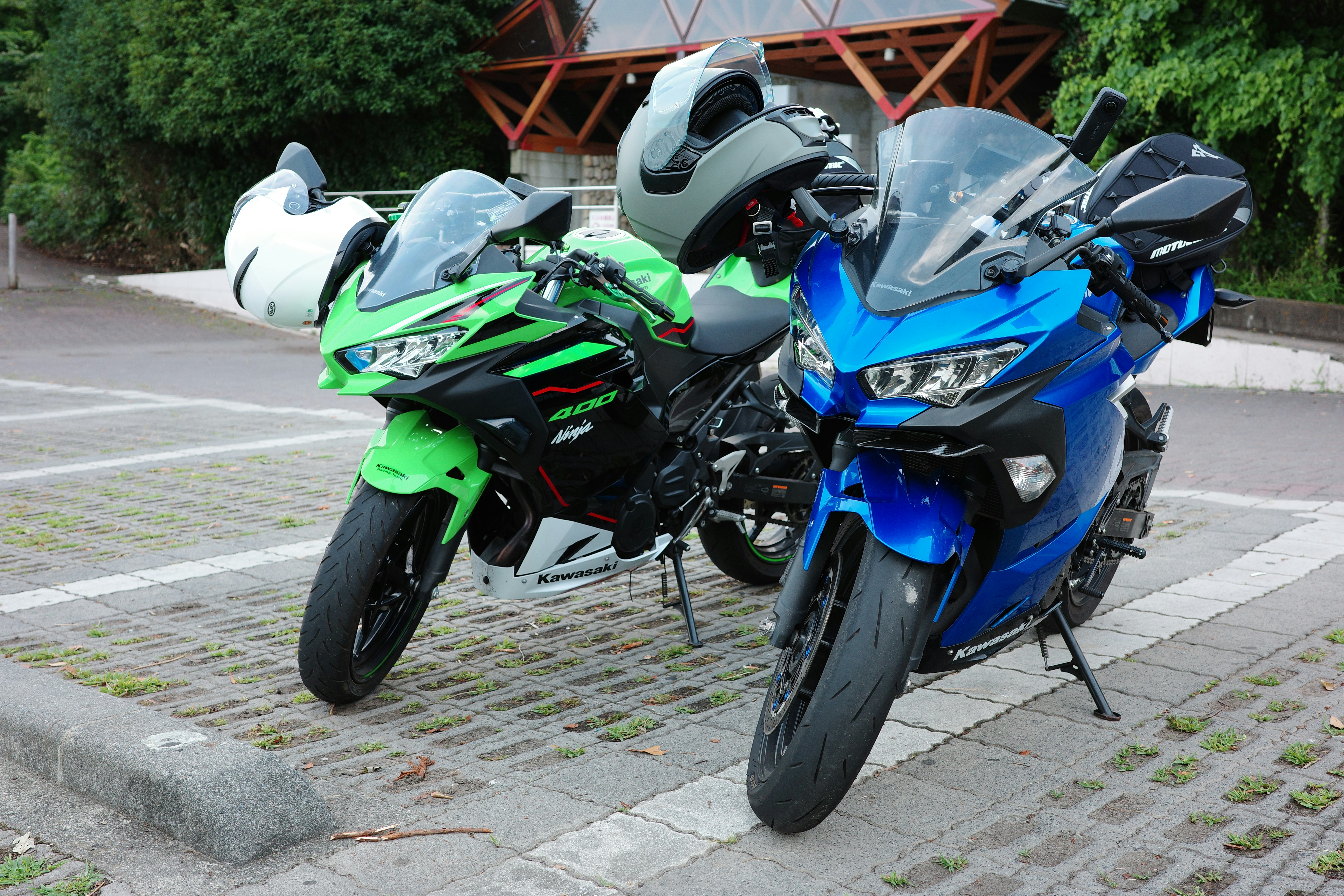 Green and blue motorcycles with helmets parked on paving