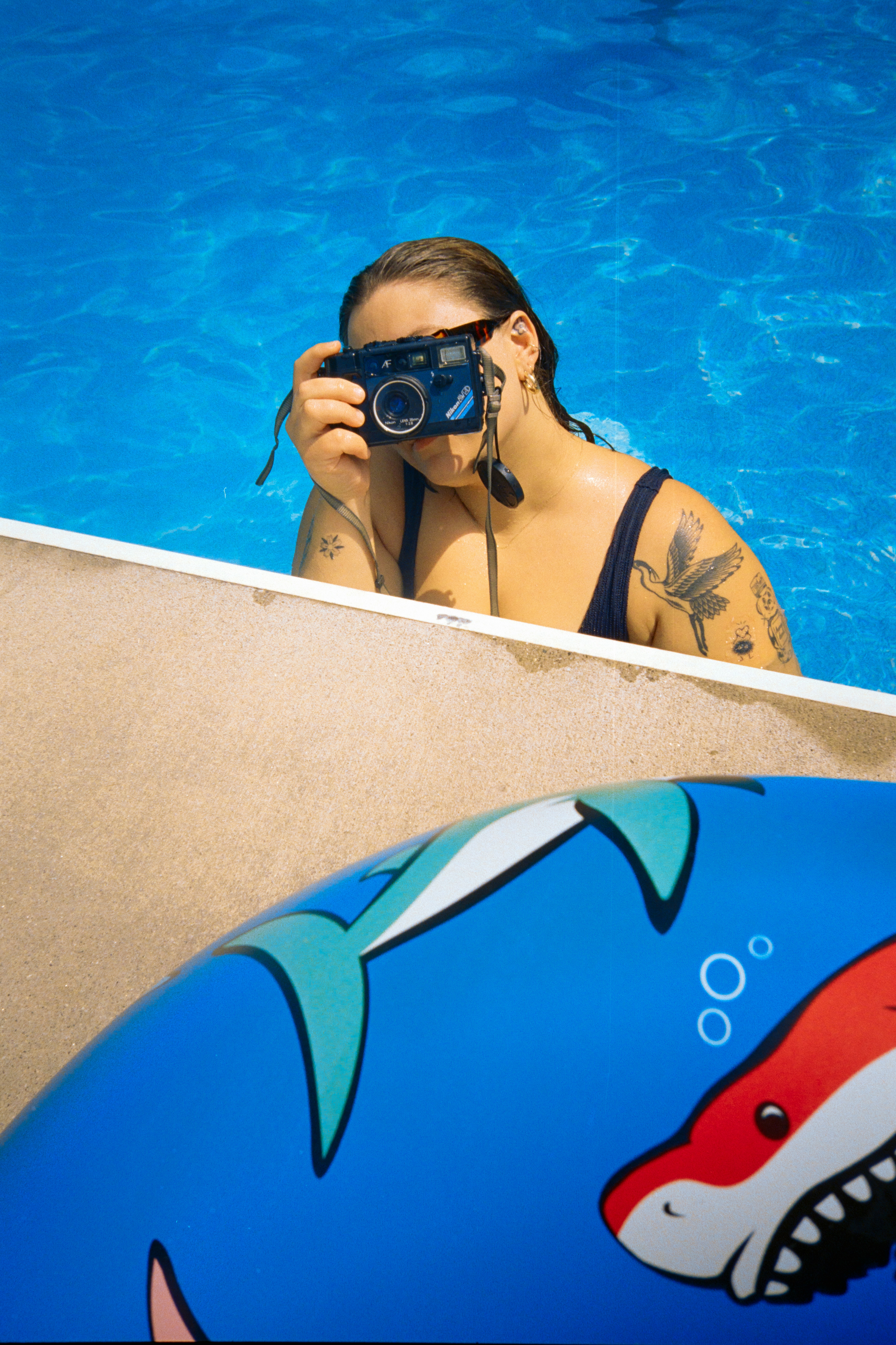 Woman in pool photographing, shark float in foreground