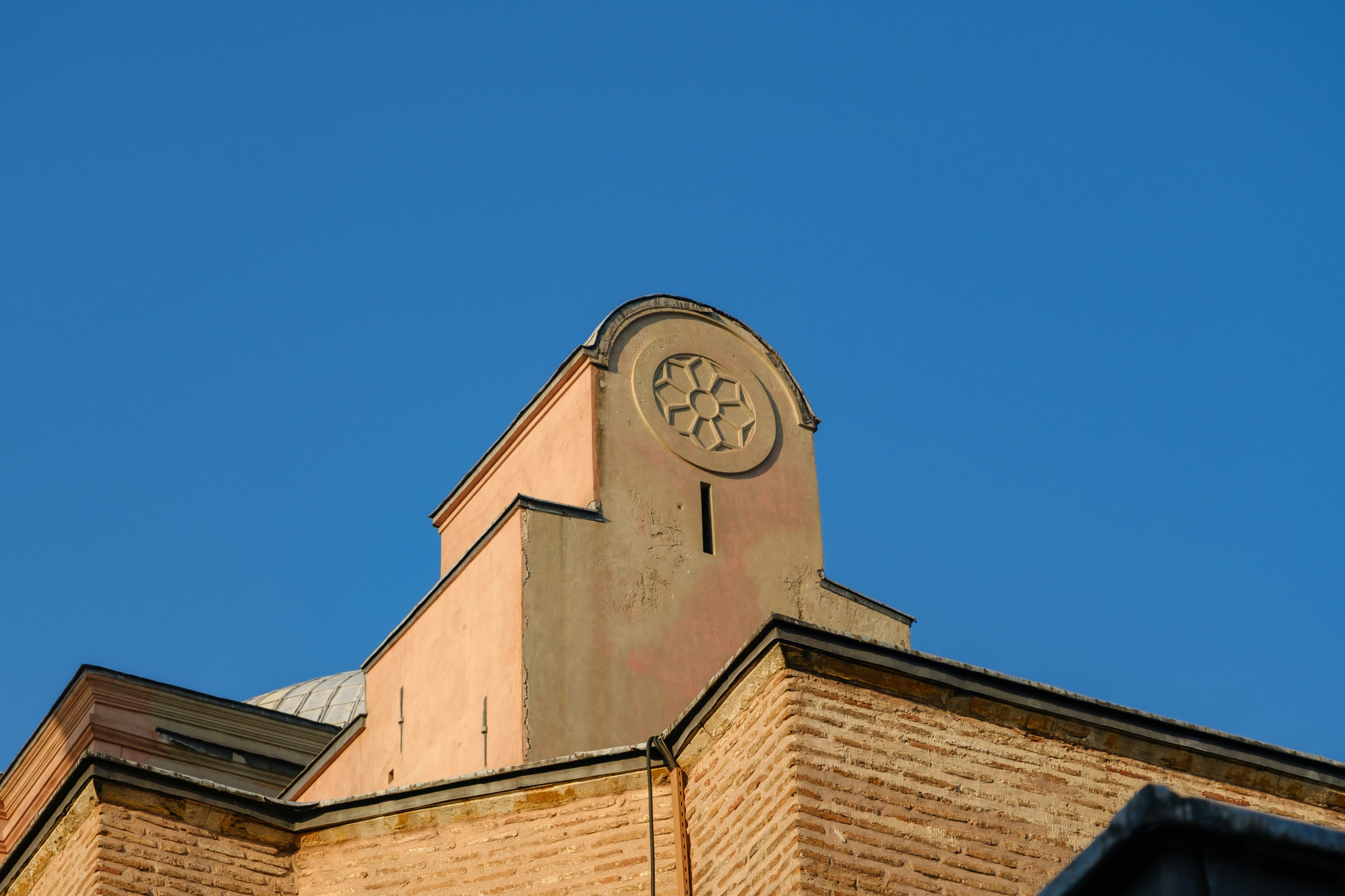 Building detail with circular ornament against clear blue sky.