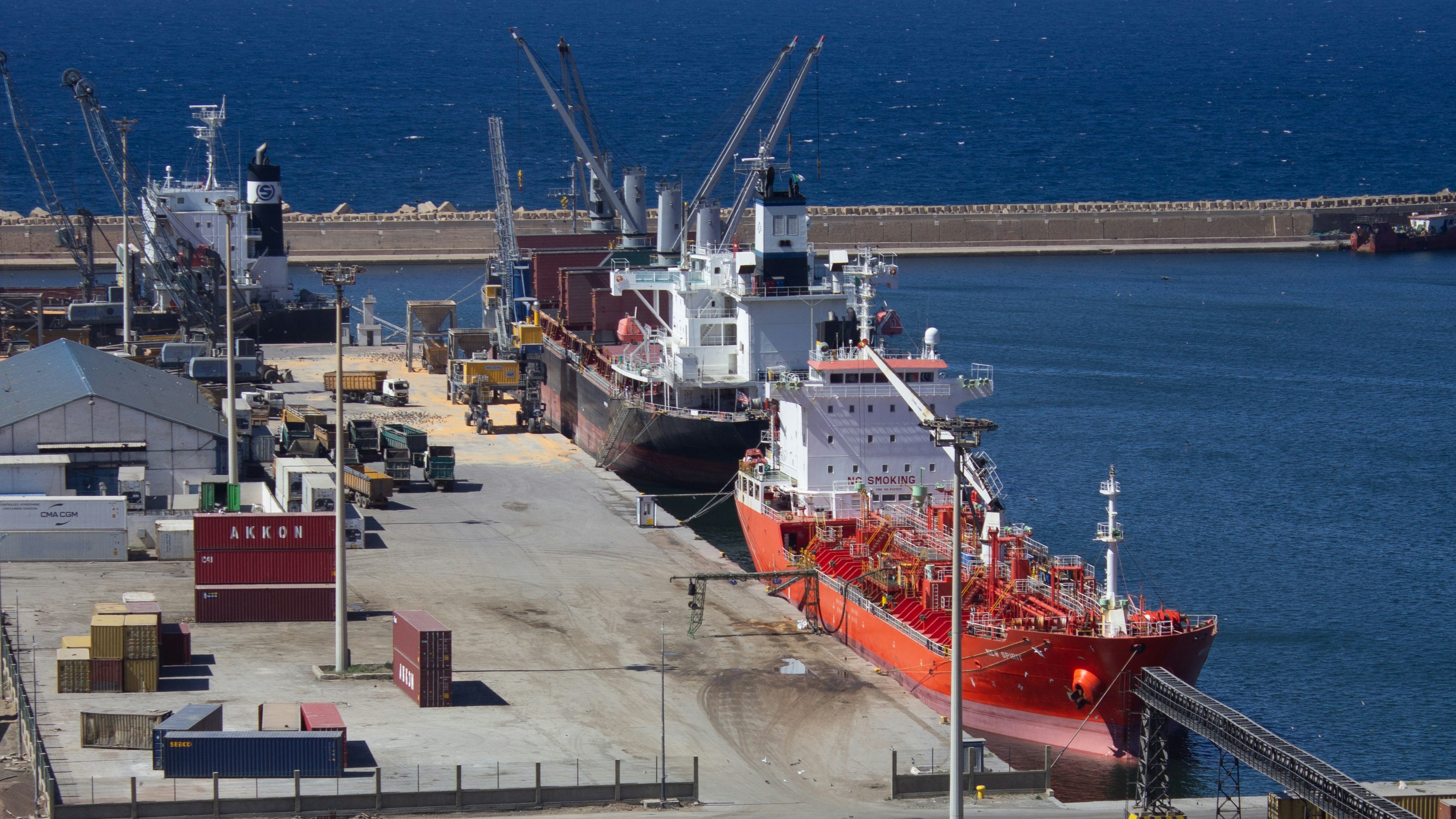 Two large ships docked at a busy port with cranes