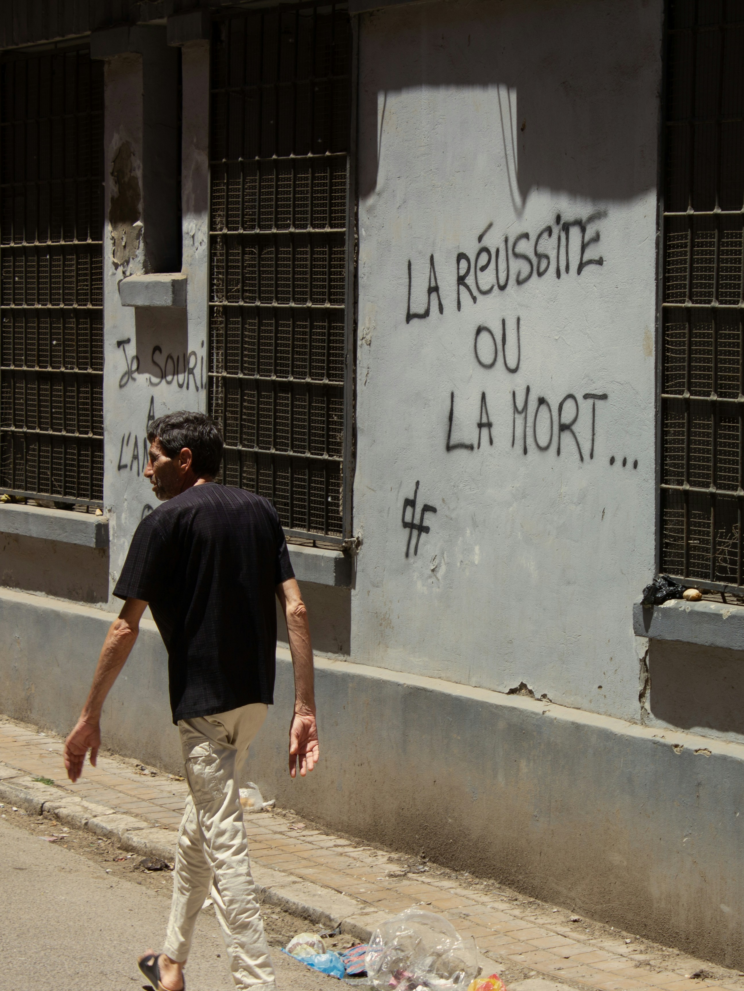 Young man walks past wall with "success or death" graffiti.
