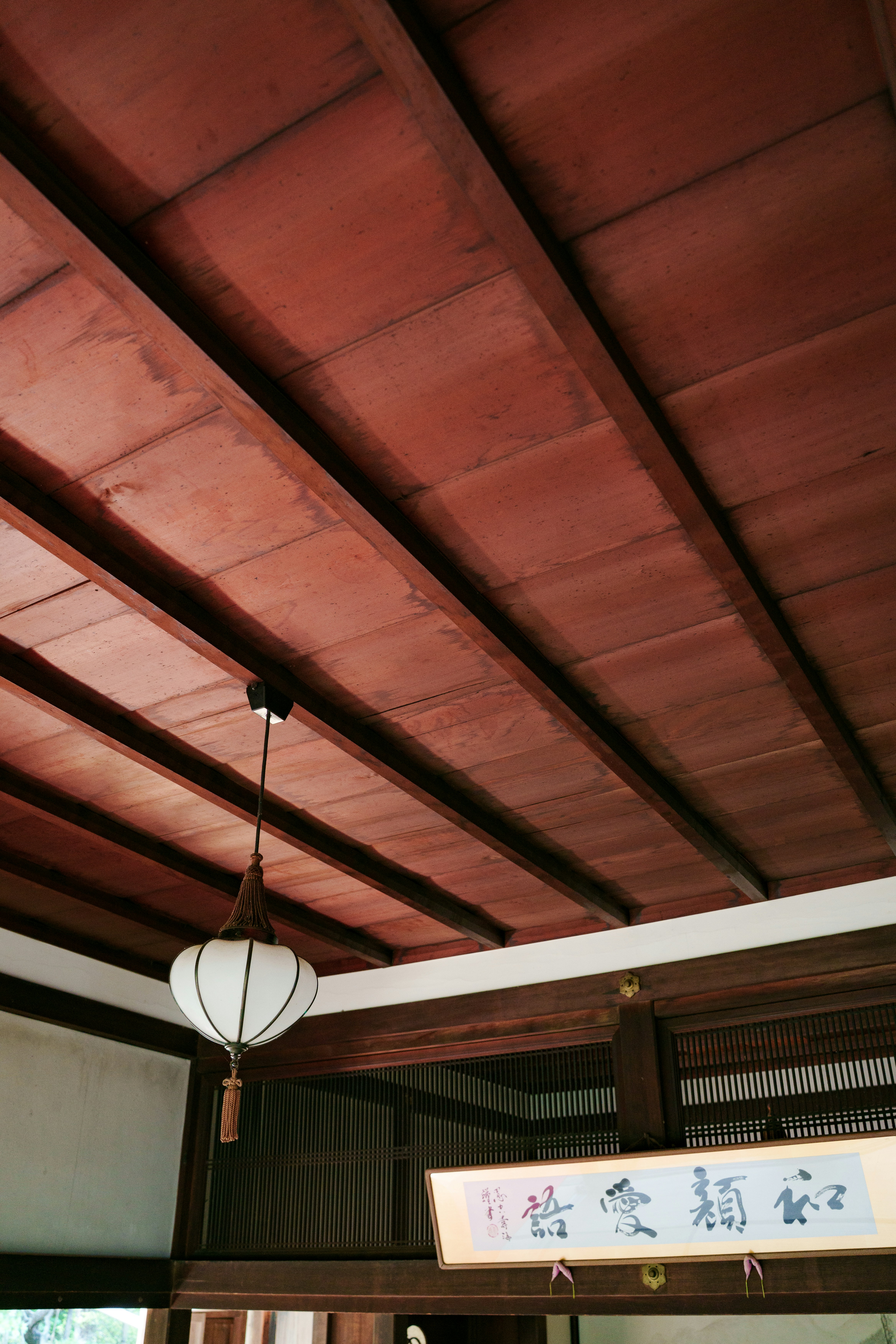 Plafond traditionnel en bois avec lanterne blanche et calligraphie.