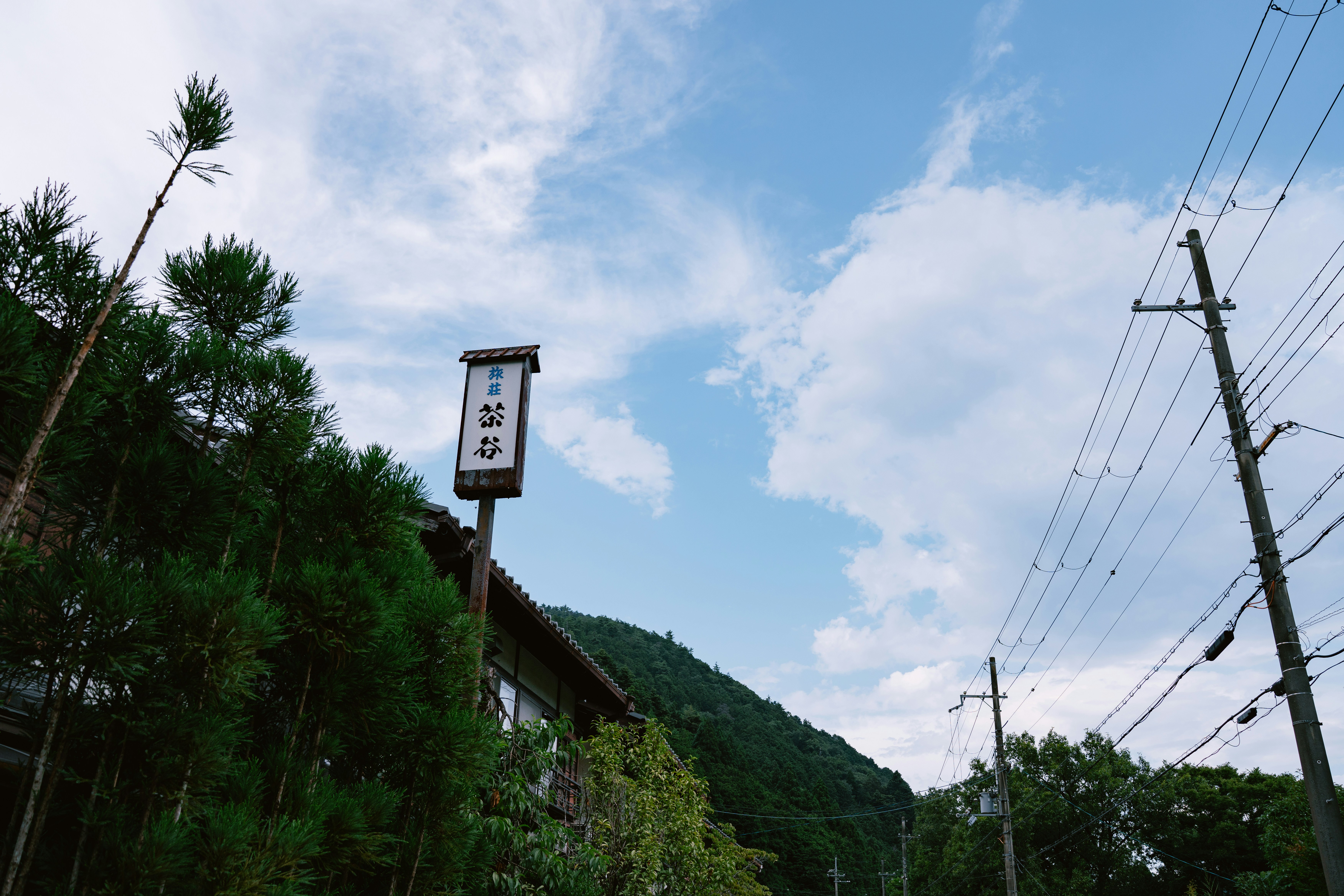 Bâtiment rural avec panneaux japonais, lignes électriques et ciel nuageux.