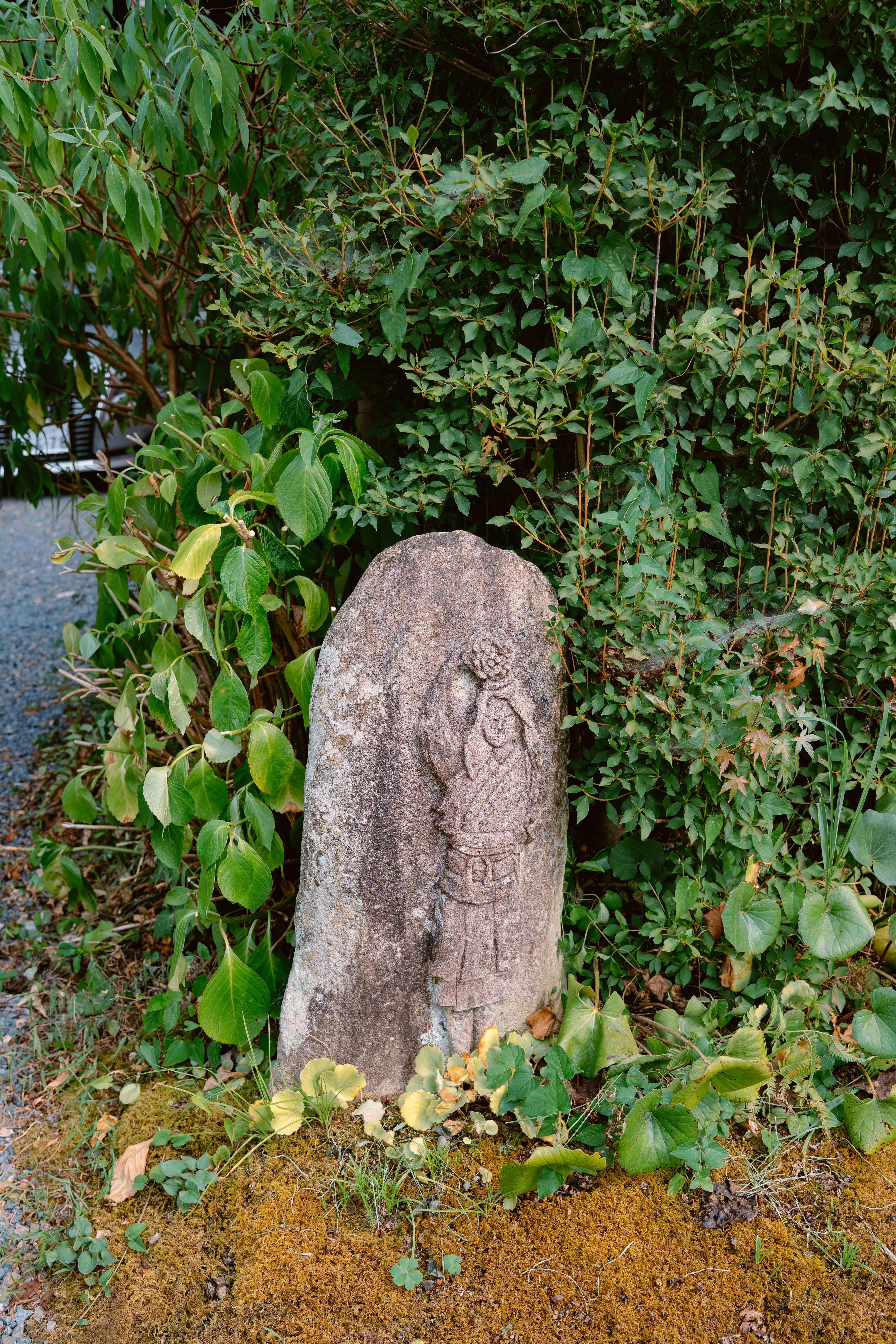 Une sculpture en pierre usée se dresse au milieu d’un feuillage vert.