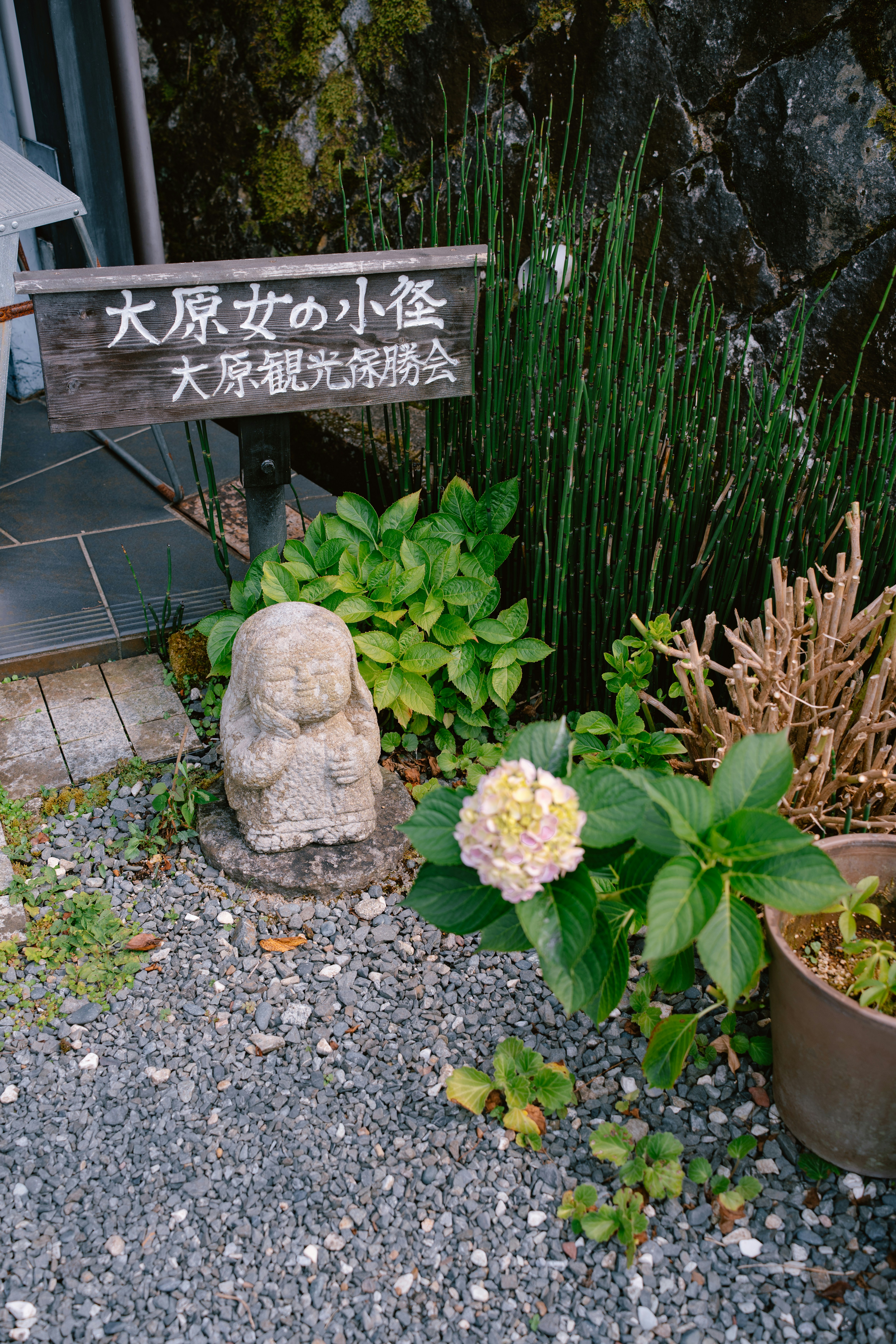 Statue en pierre, panneau japonais et plantes dans un jardin.