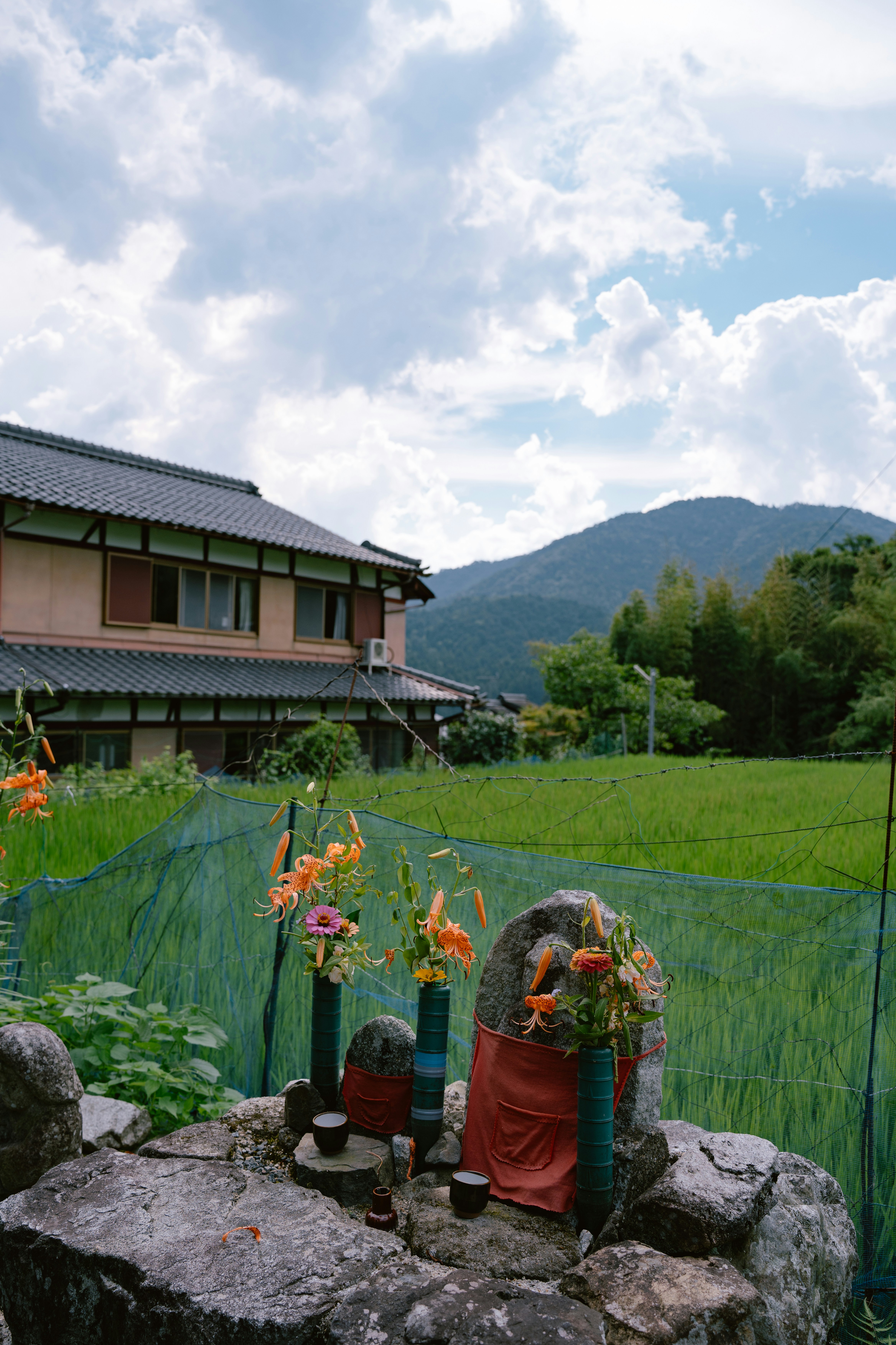 Statues de jizo en pierre avec des fleurs dans un paysage rural japonais.