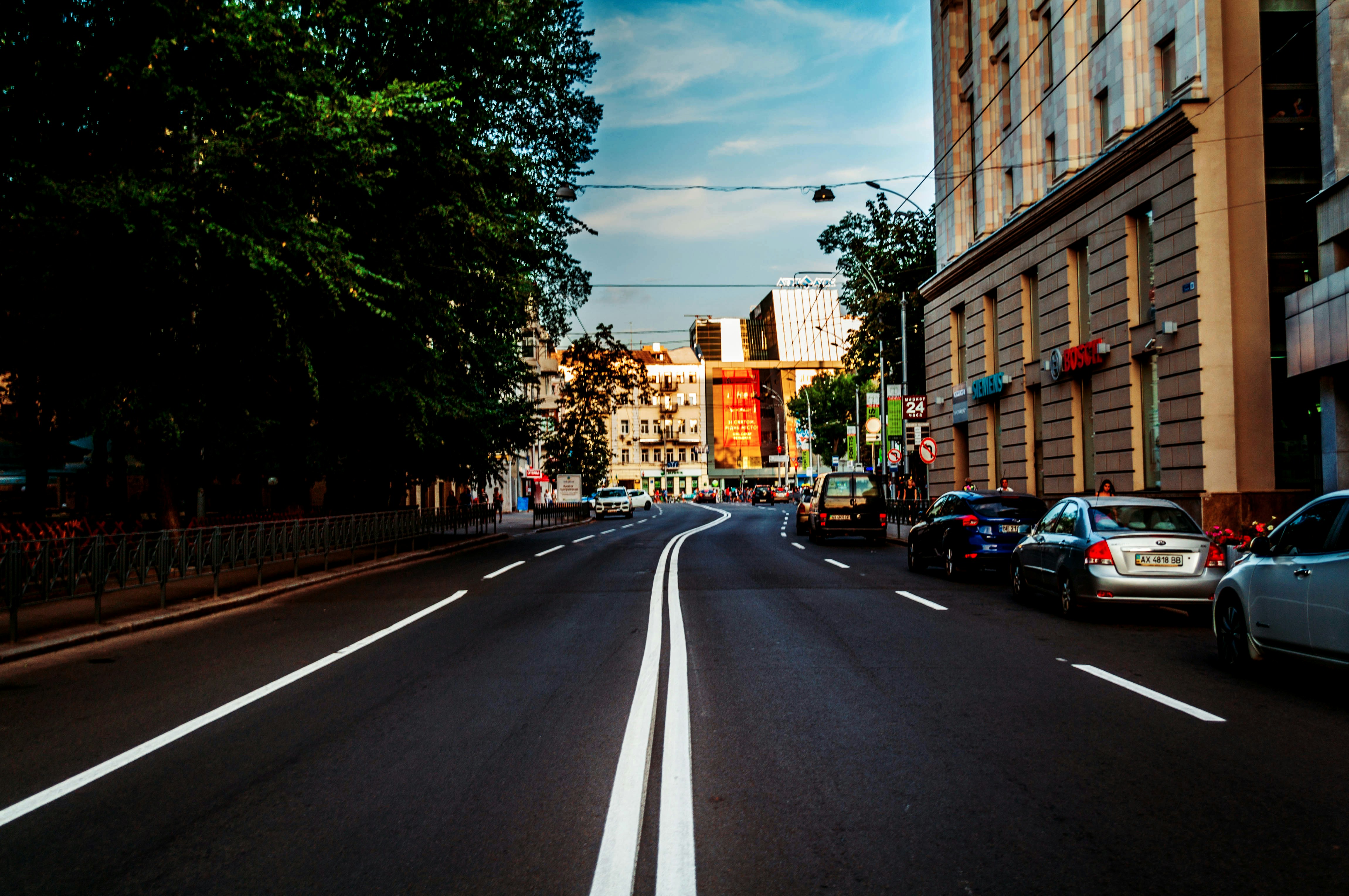 Urban street scene with buildings, parked cars, and trees.