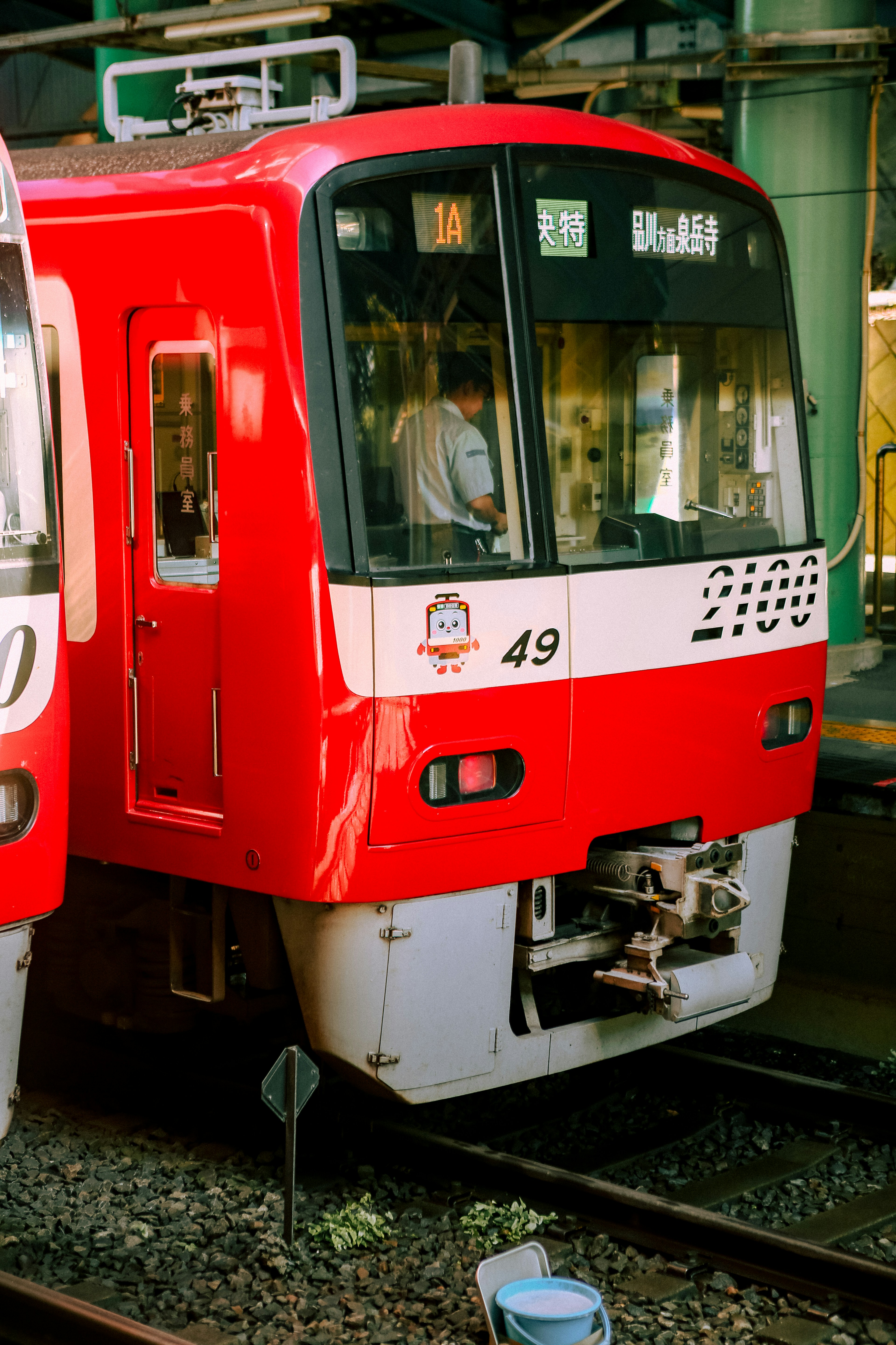 A red train with a driver at a station platform.