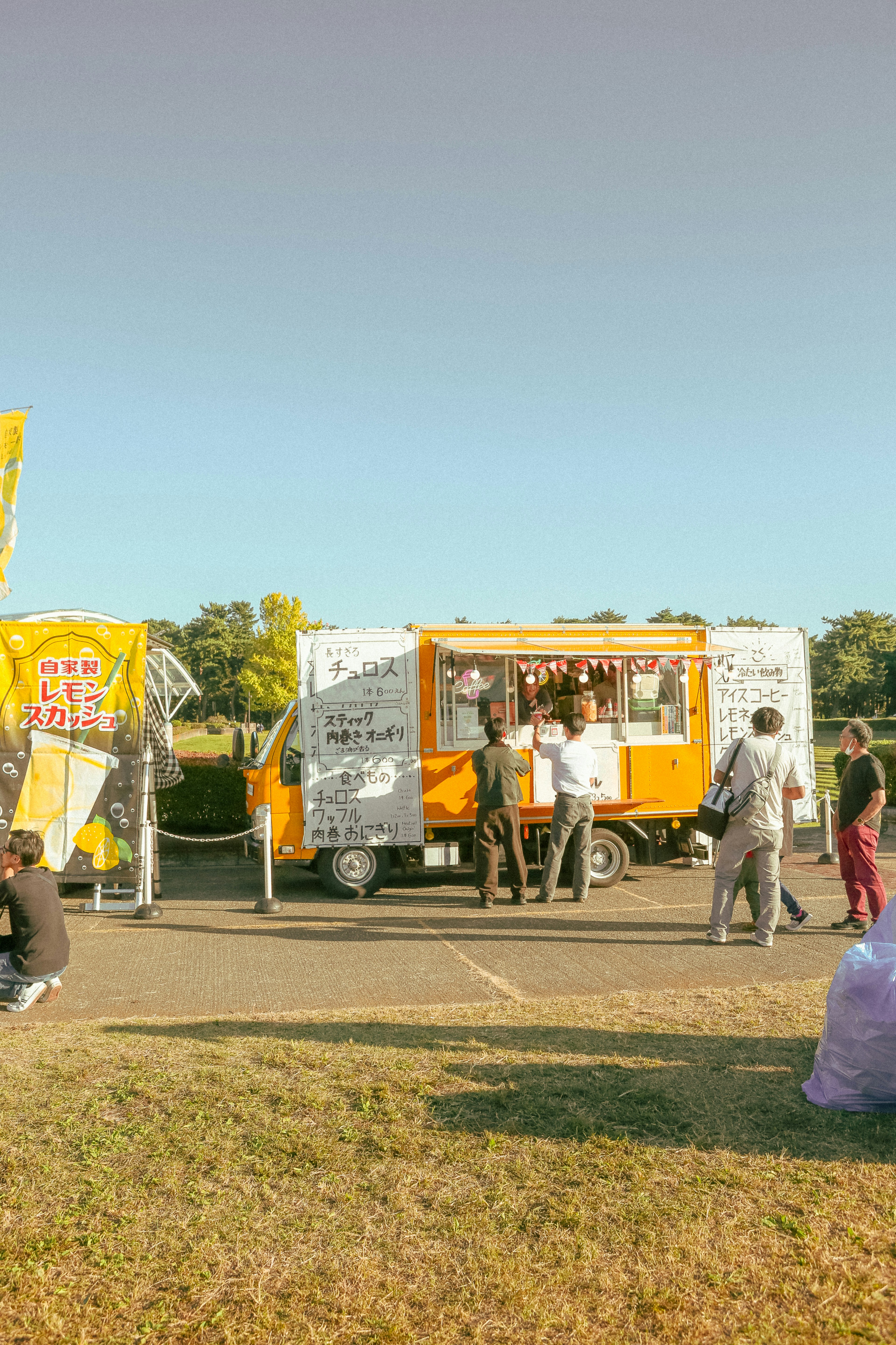 An orange food truck with customers at an outdoor event.