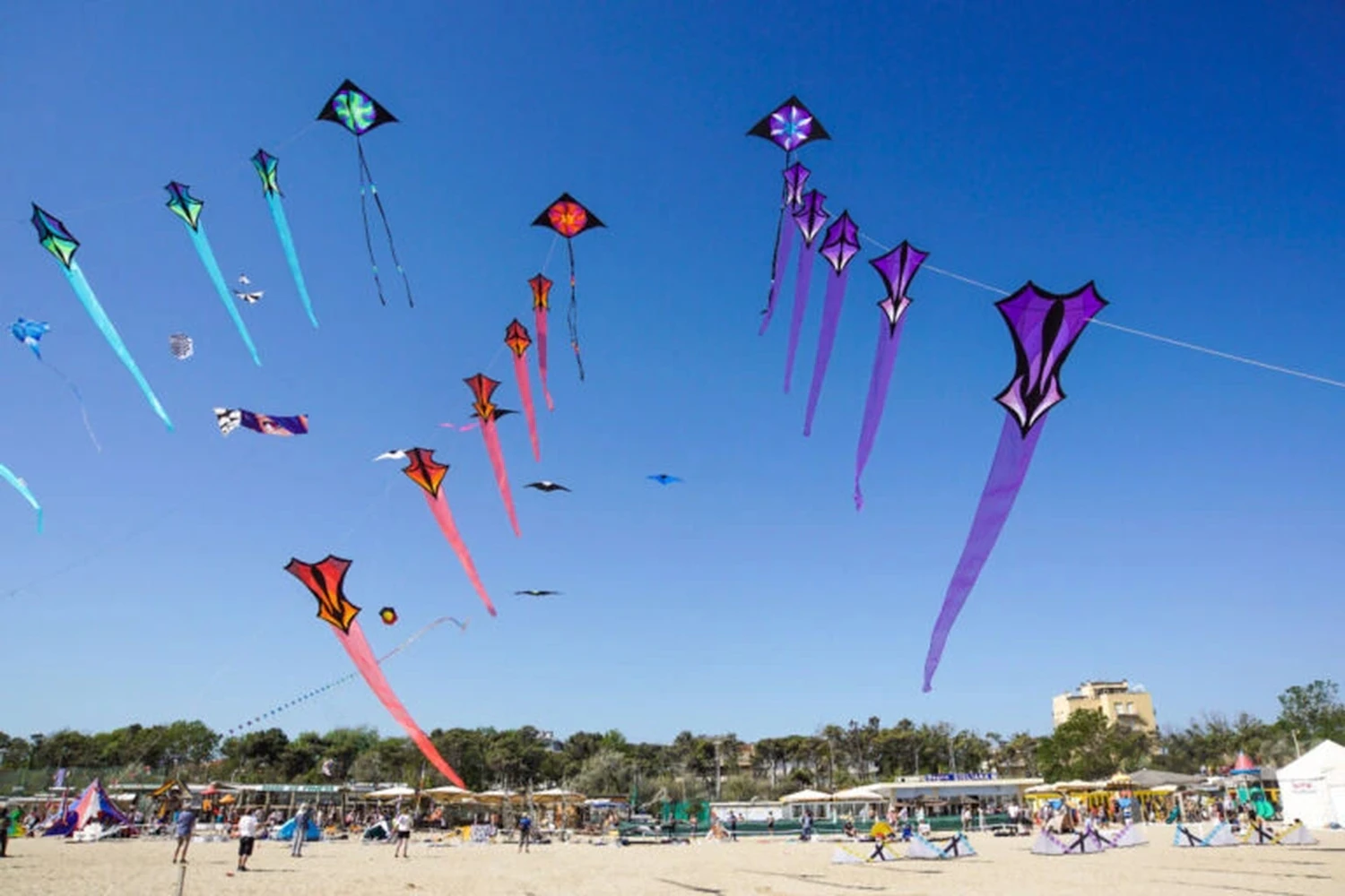 Colourful kites flying high over a sandy beach full of people