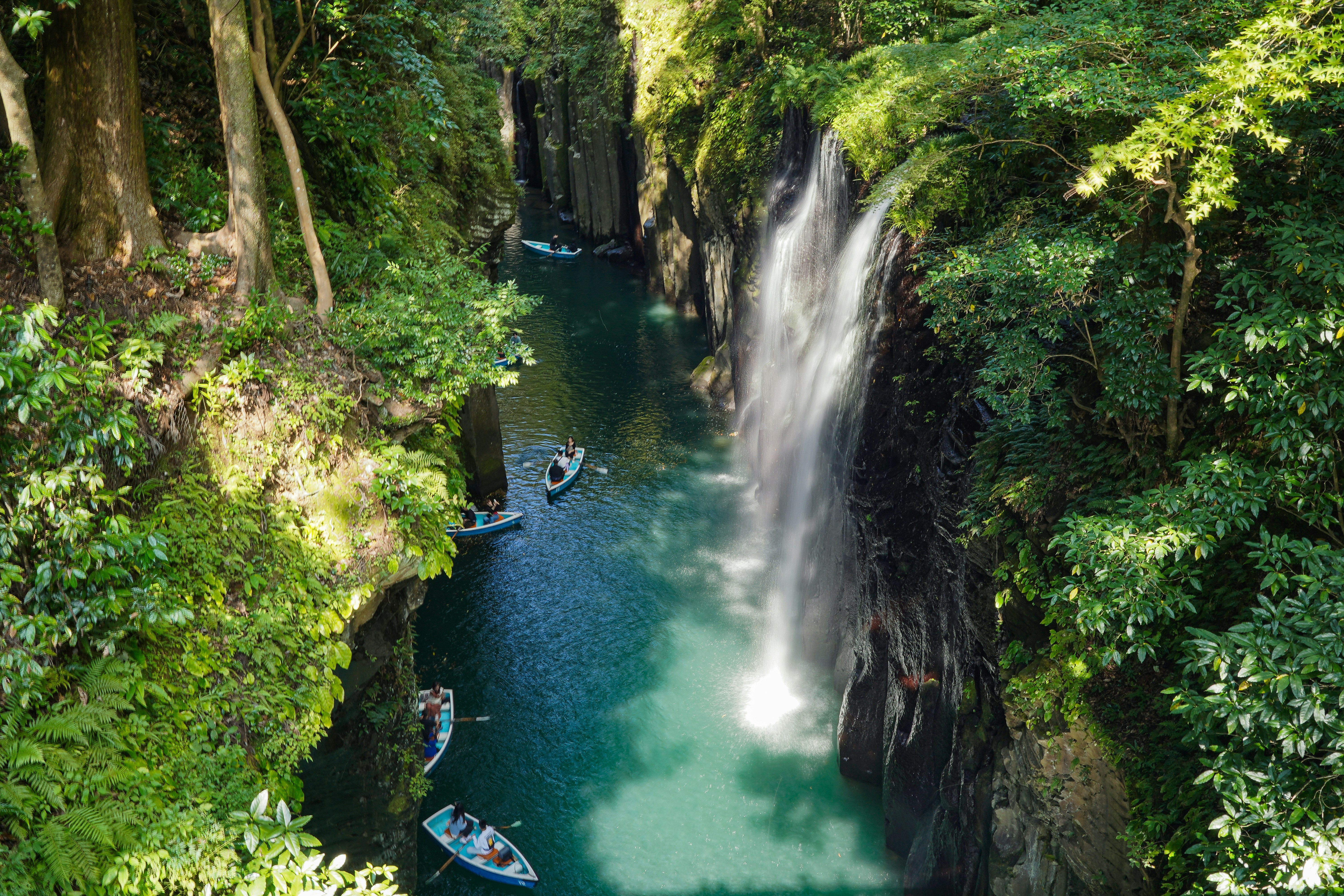 Lush gorge with waterfall and boats on turquoise river