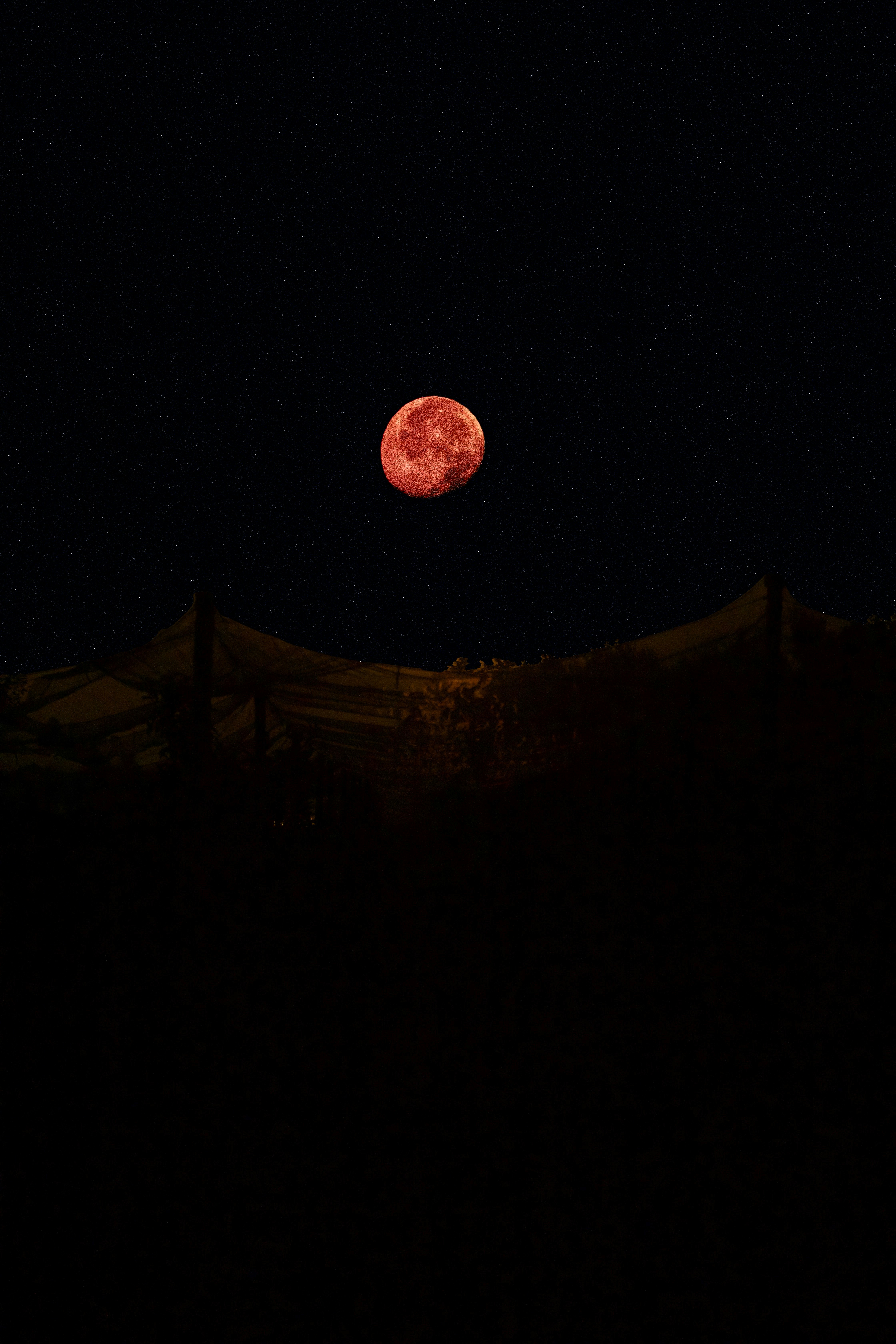 Blood moon over dark mountains under a starry night.