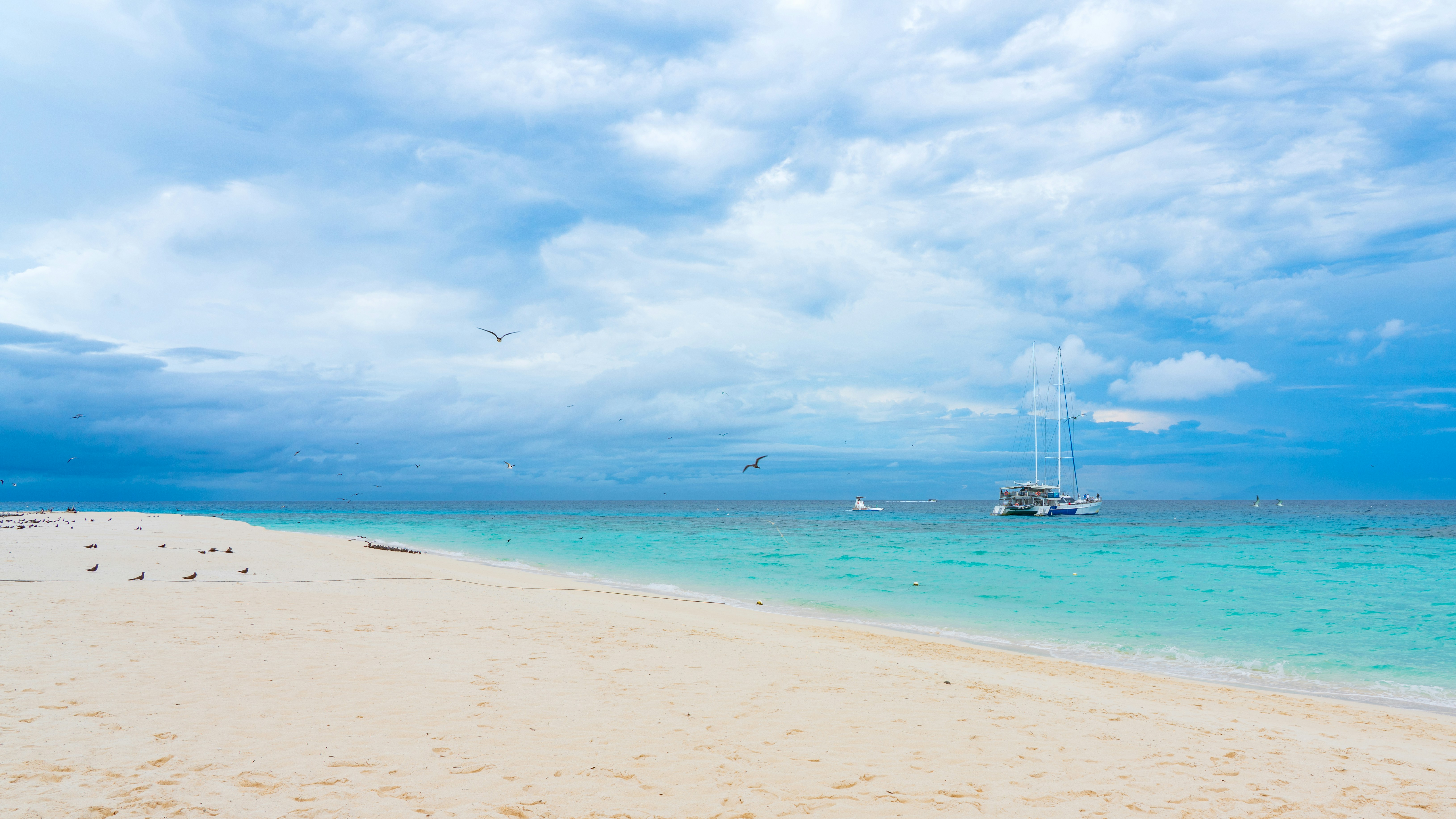 White sand beach, turquoise ocean, cloudy sky, catamaran